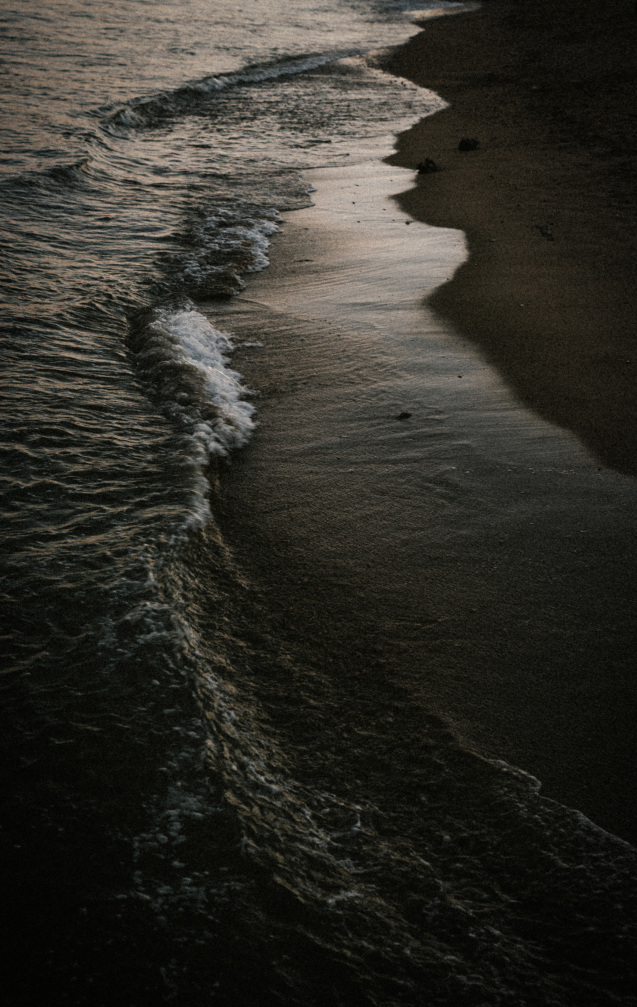 Surf breaking across dark sand