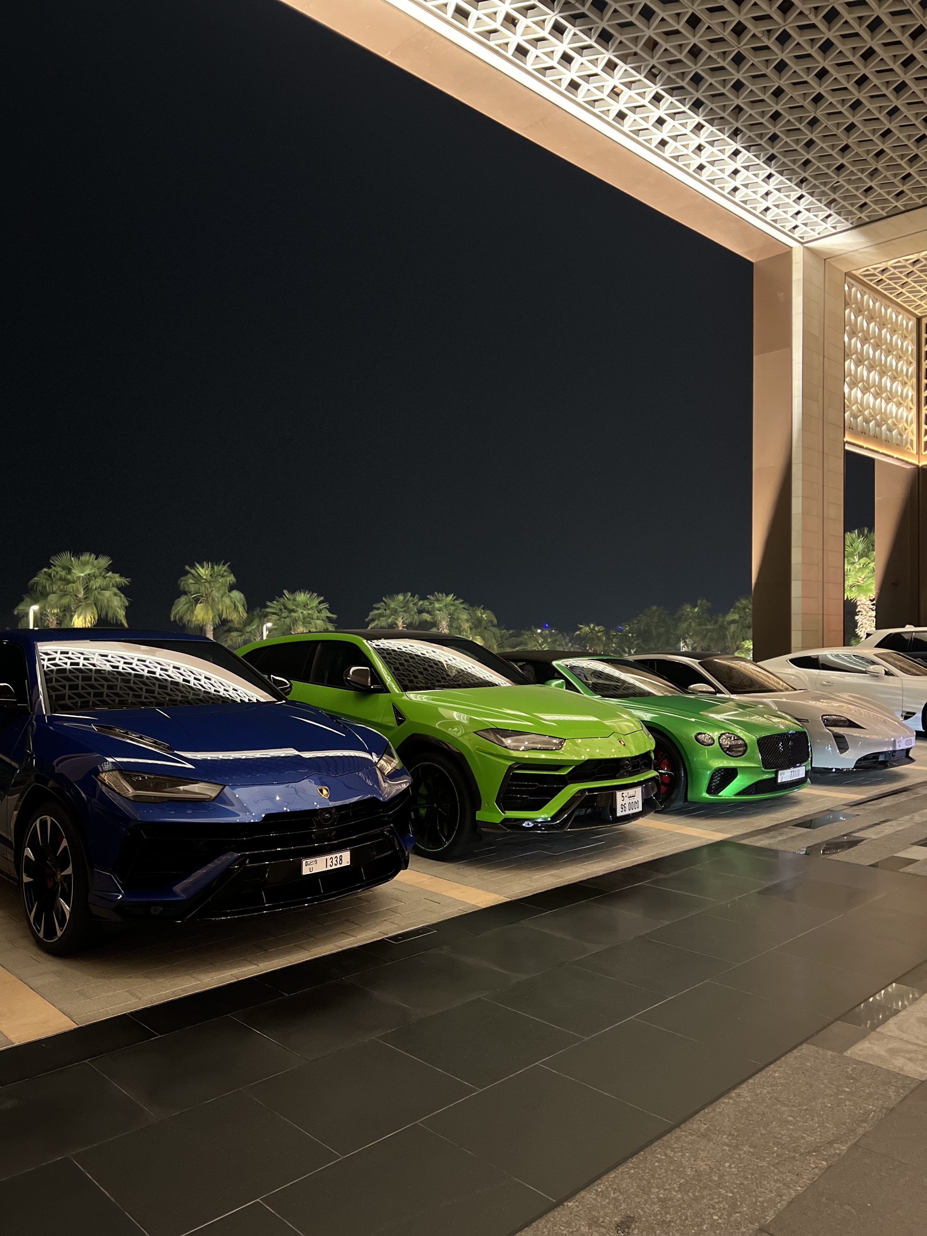 Row of supercars including blue and green Lamborghini and Bentley parked at night outside Atlantis The Royal, Dubai