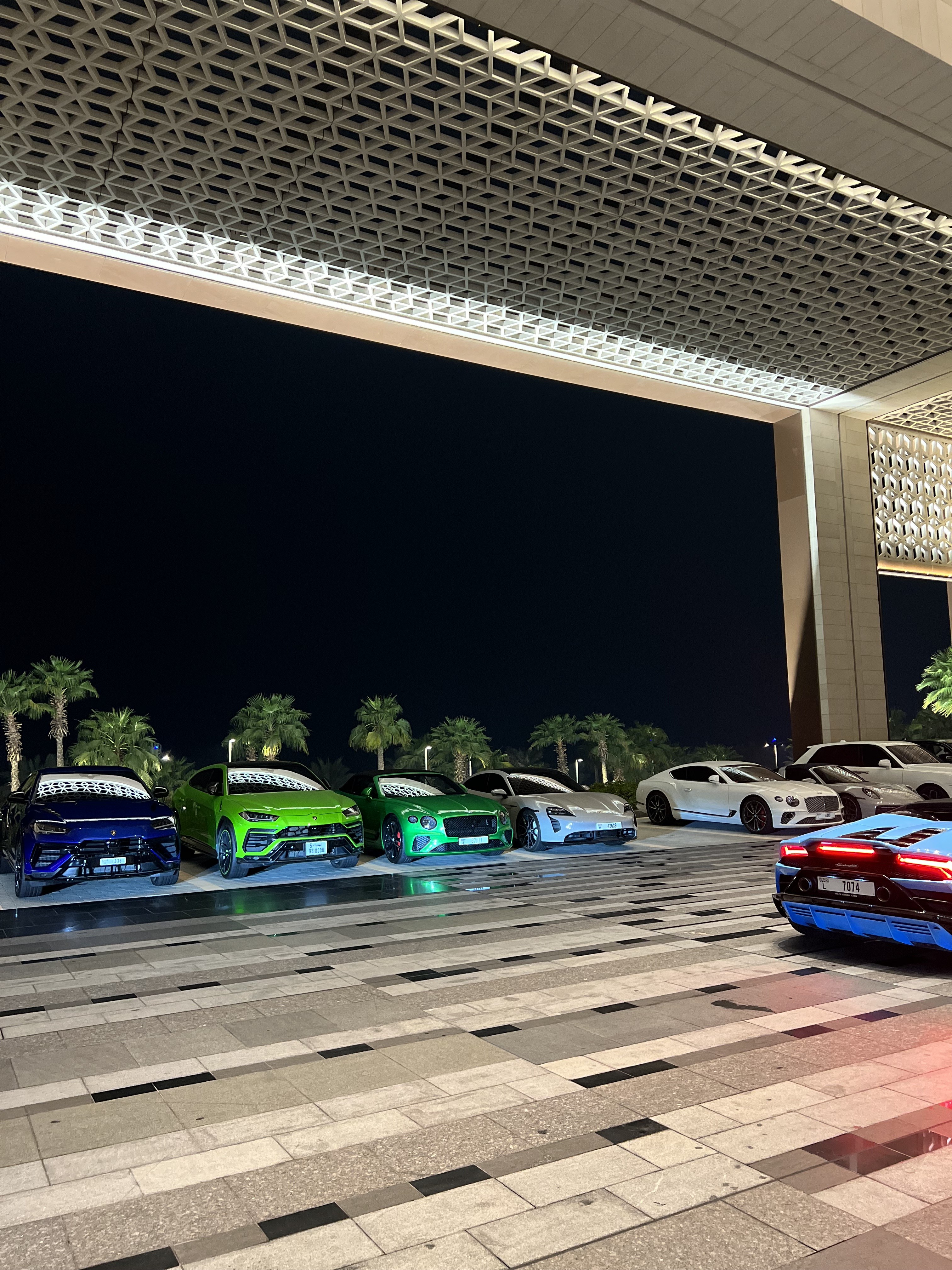 Supercars lined along the forecourt beneath geometric lattice canopy at night, Atlantis The Royal, Dubai
