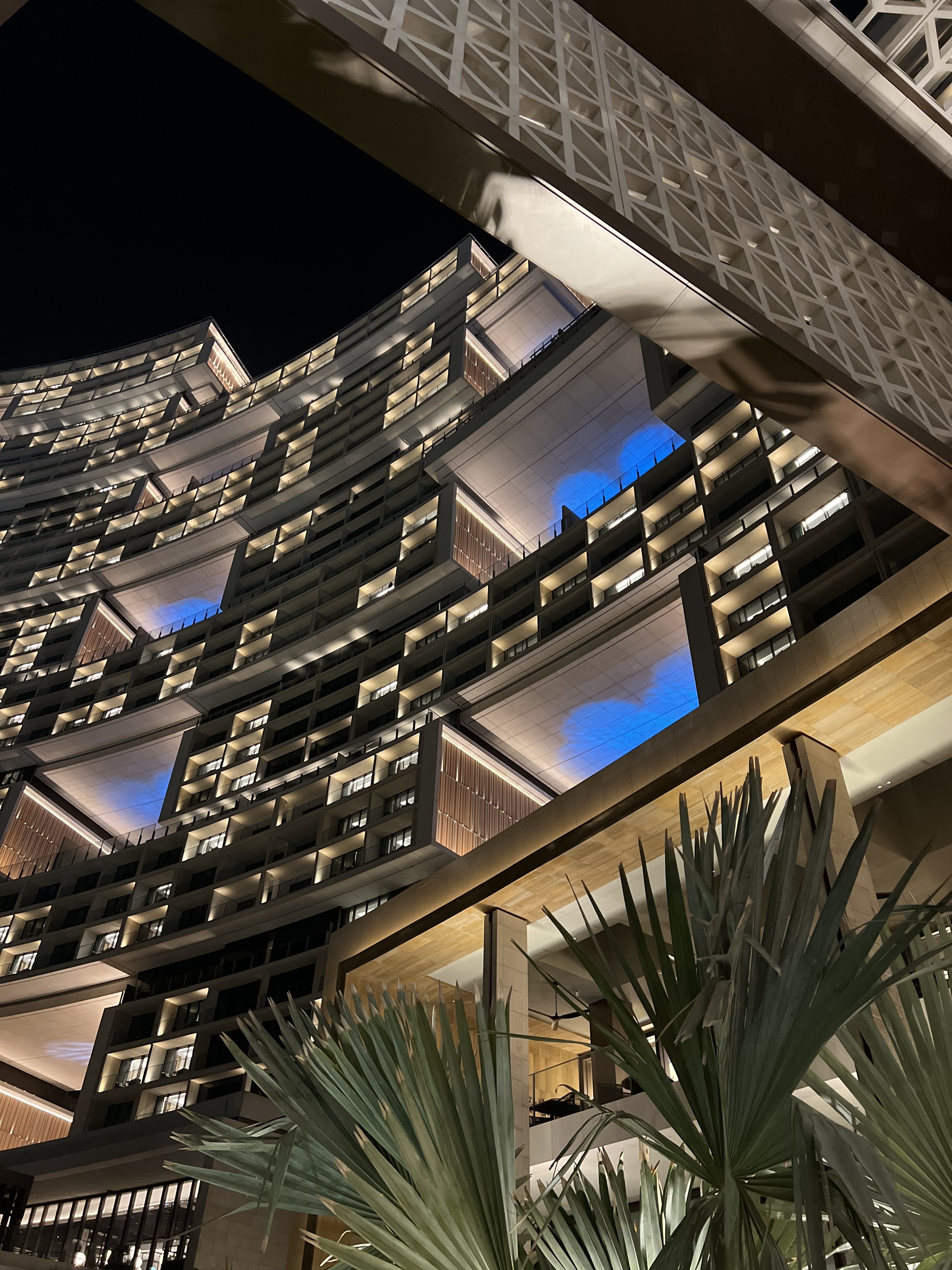 Curved hotel facade at night with stacked lit balconies and blue upper lighting, Atlantis The Royal, Dubai