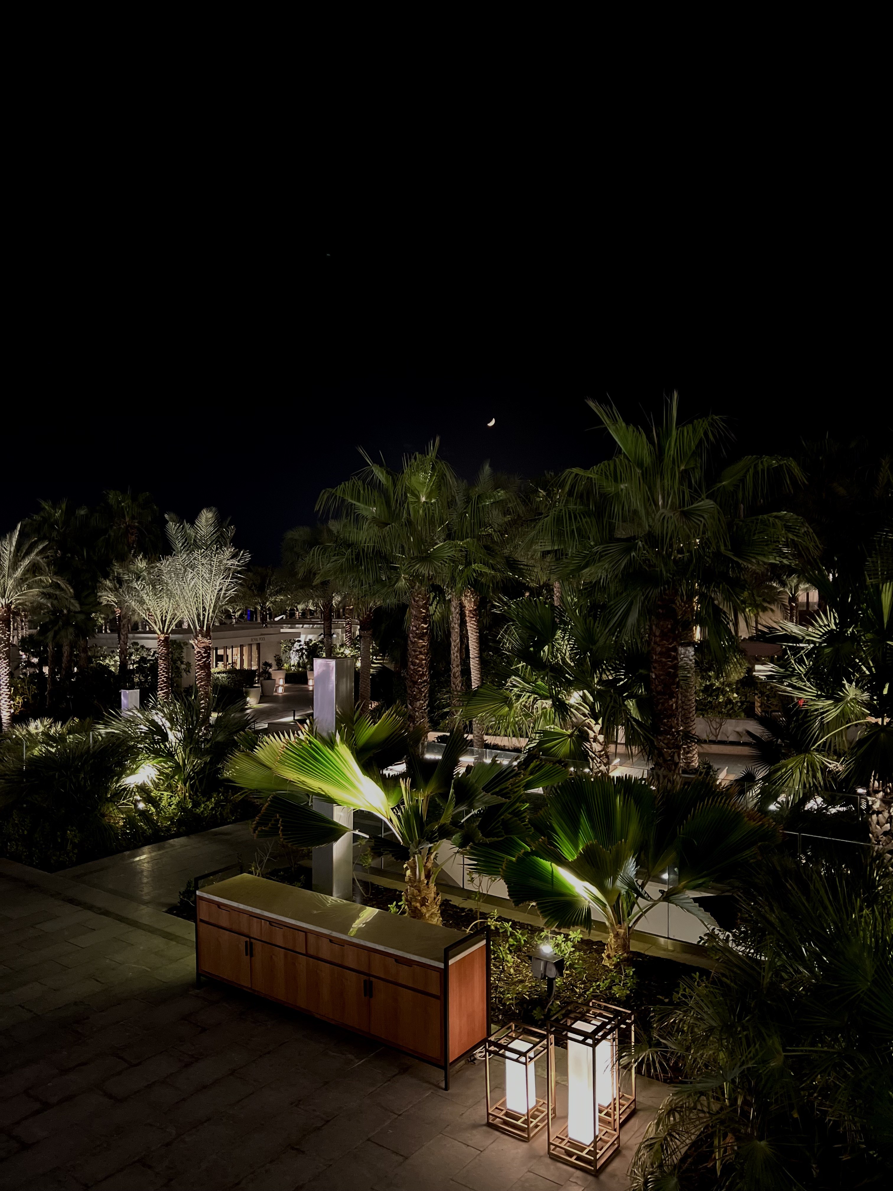 Palm gardens lit from below at night with square lanterns and crescent moon above, Atlantis The Royal, Dubai