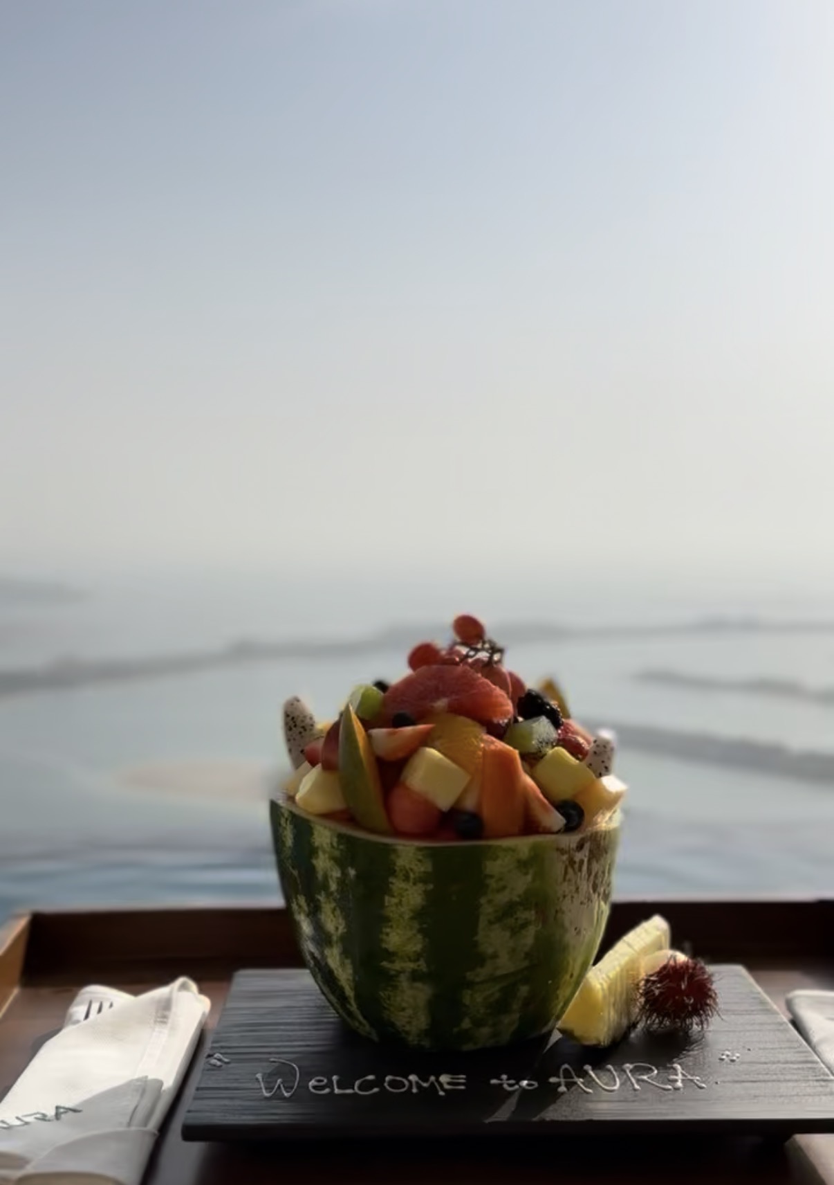 Welcome to AURA fruit bowl on tray, hazy sea horizon, Dubai