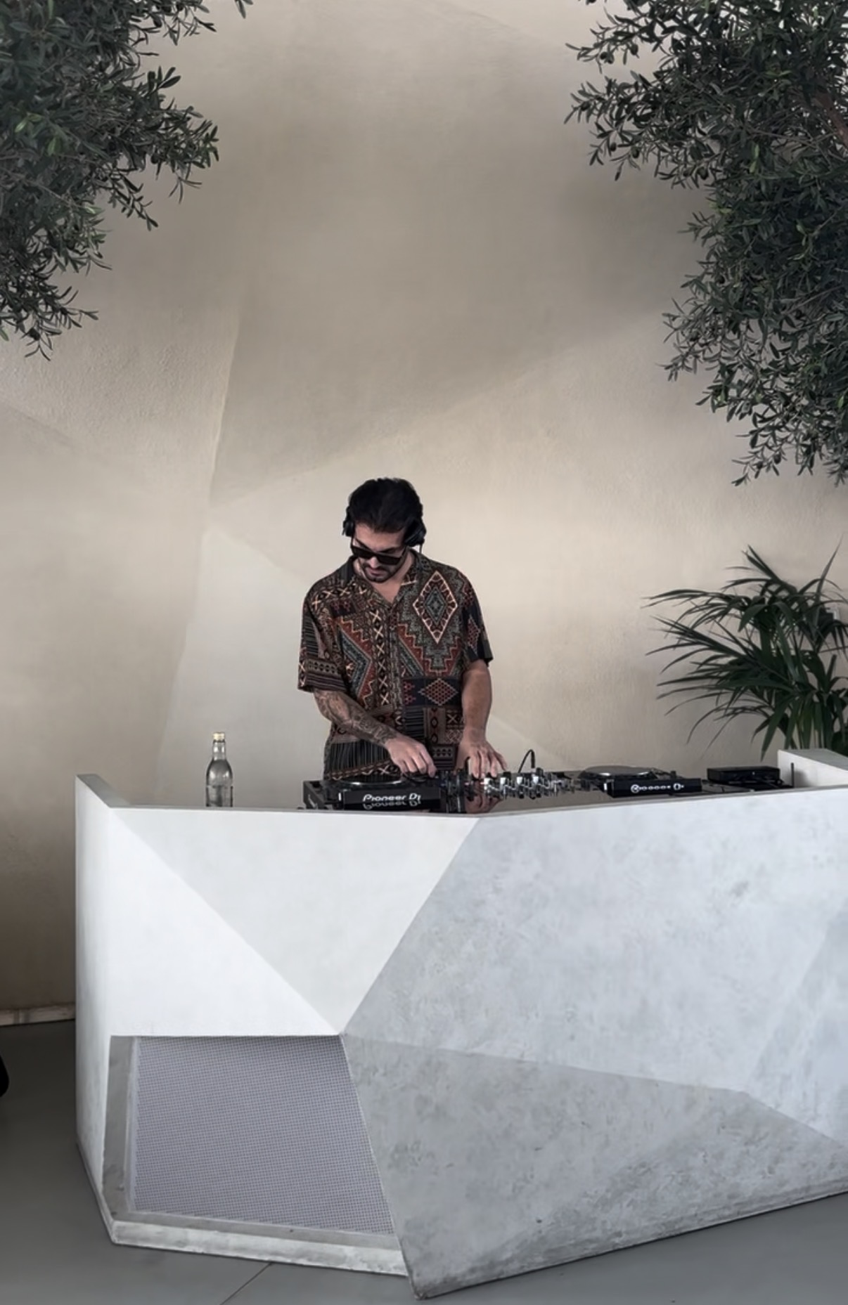DJ at geometric booth beneath olive trees, AURA, Dubai