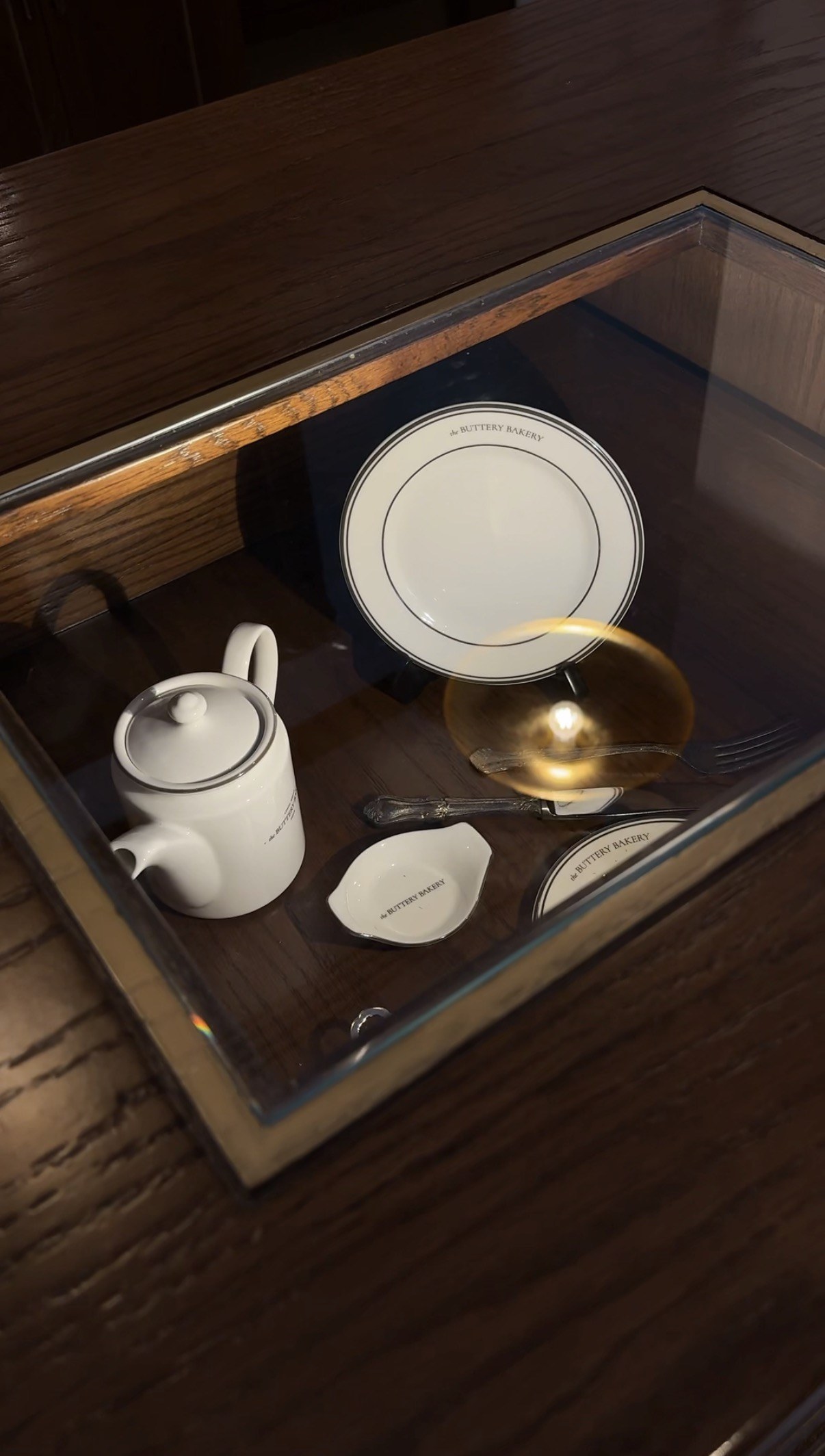 Branded teapot and plates in a glass cabinet, The Buttery Bakery, Doha
