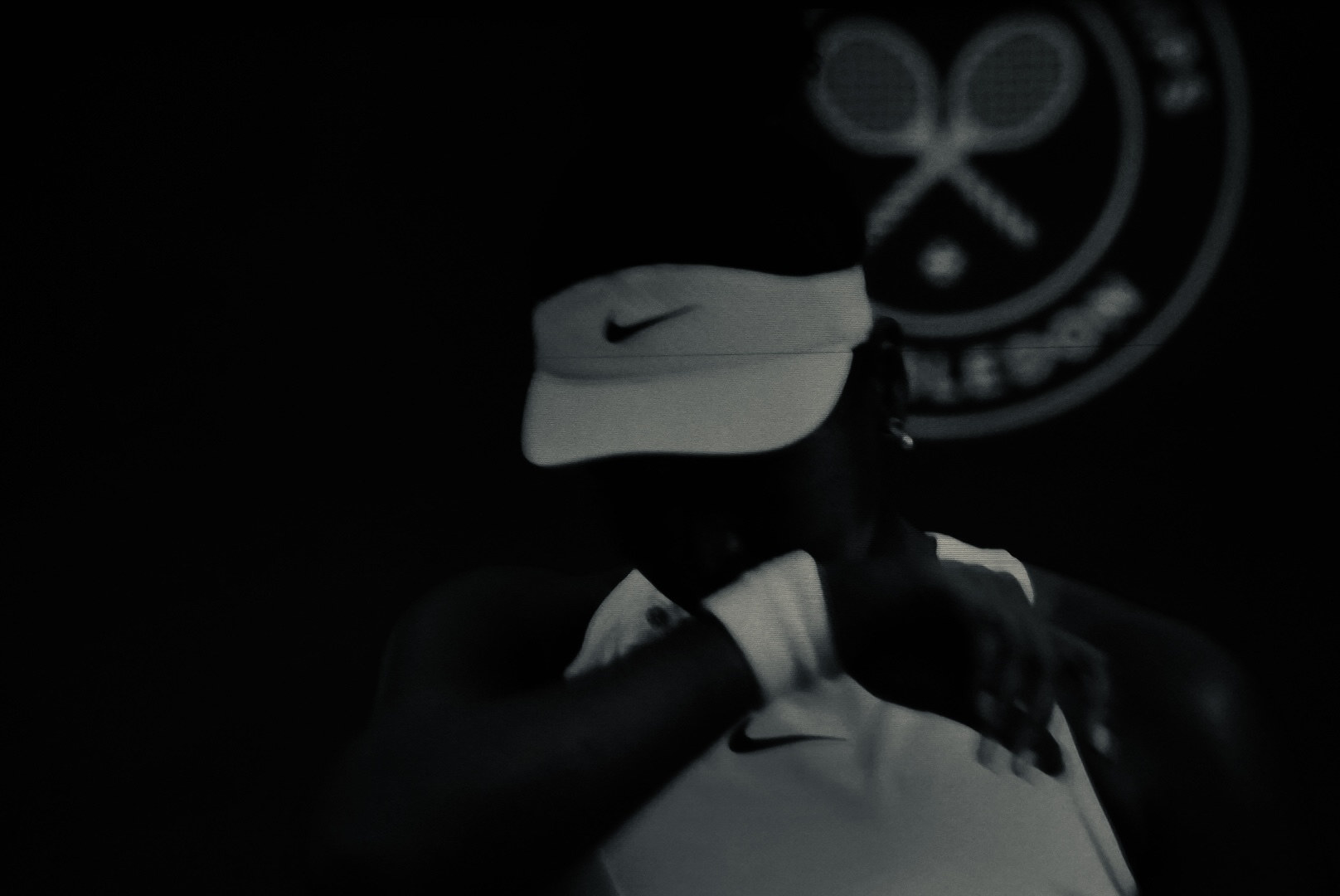 A player wiping their face with a wristband, visor low, between points