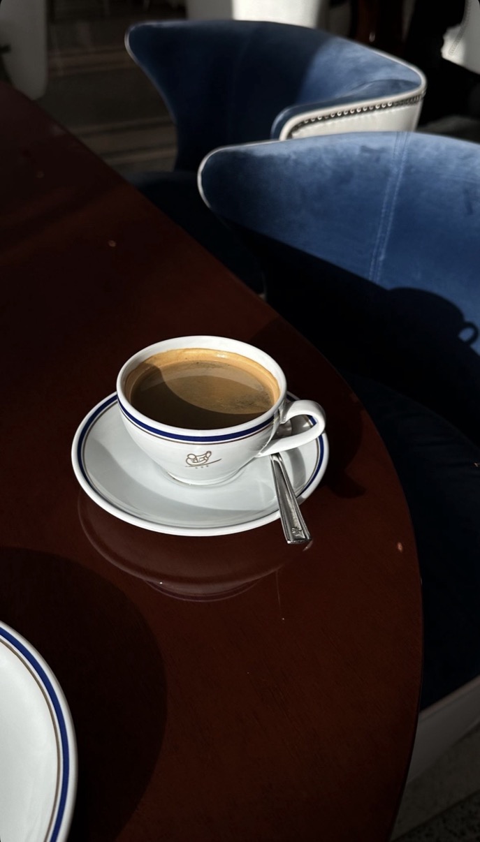 Branded white coffee cup on a polished dark wood table beside blue velvet seating, Cipriani Dolci, Doha