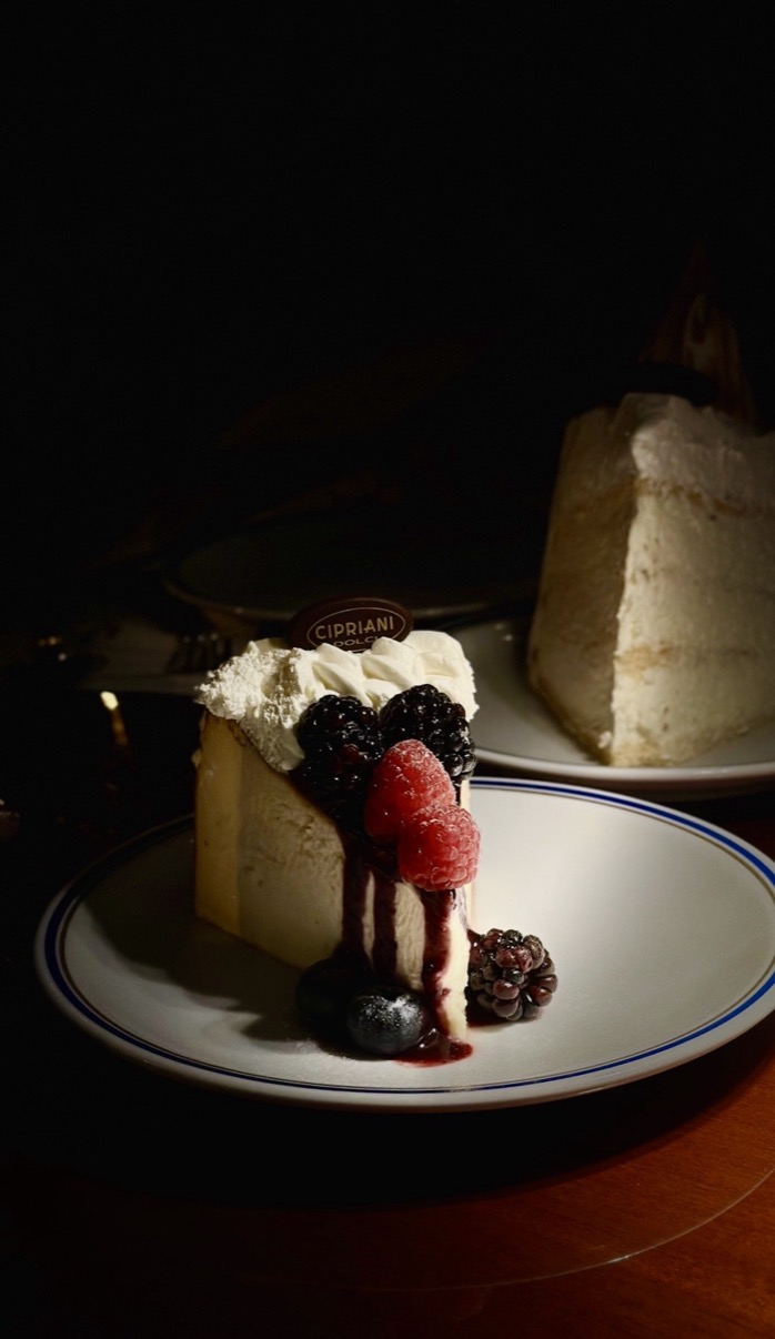 Cheesecake slice with berries on a blue-rimmed Cipriani plate in low light, Cipriani Dolci, Doha