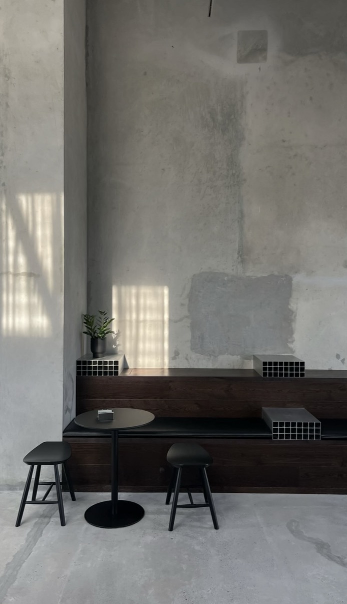 Bare concrete café interior with light bars on the wall, dark wooden bench, Dubai