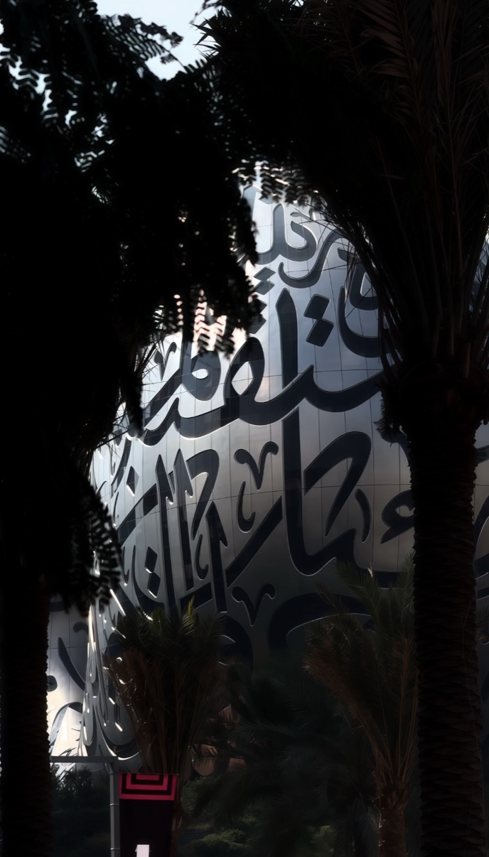 Large Arabic calligraphy facade seen through silhouetted palm trees, Dubai