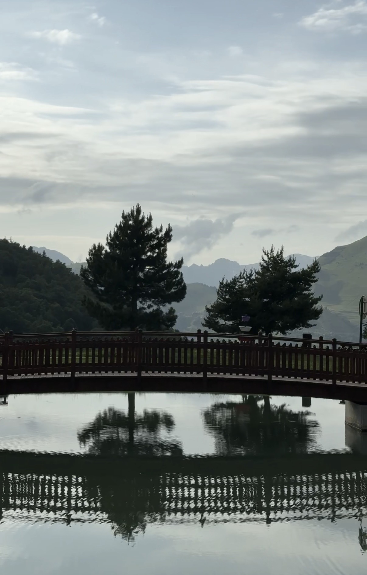 Wooden bridge over still lake with mountains behind, French Alps