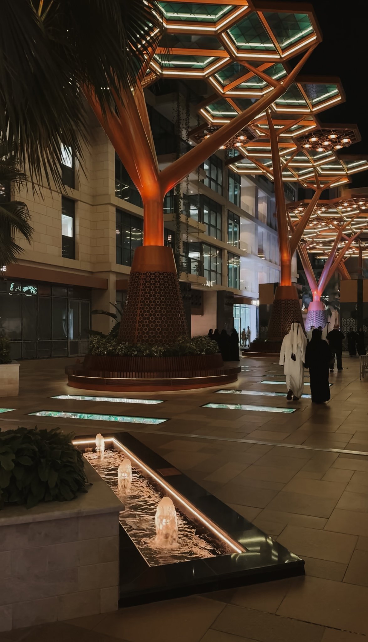 A fountain channel running down the promenade beneath lit canopies, Gewan Island, Doha