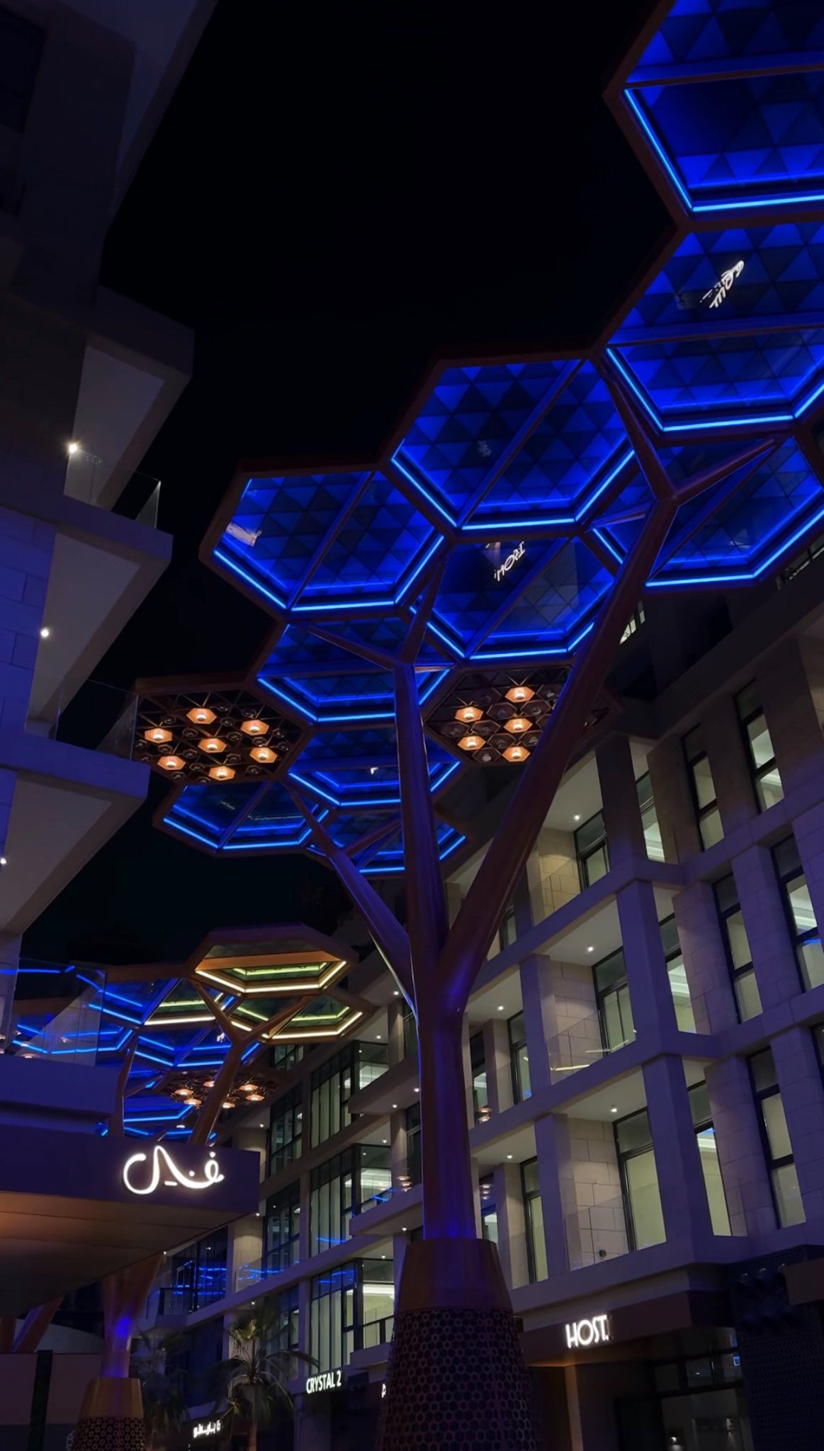 A hexagonal canopy lit blue against the apartment facades, Gewan Island, Doha