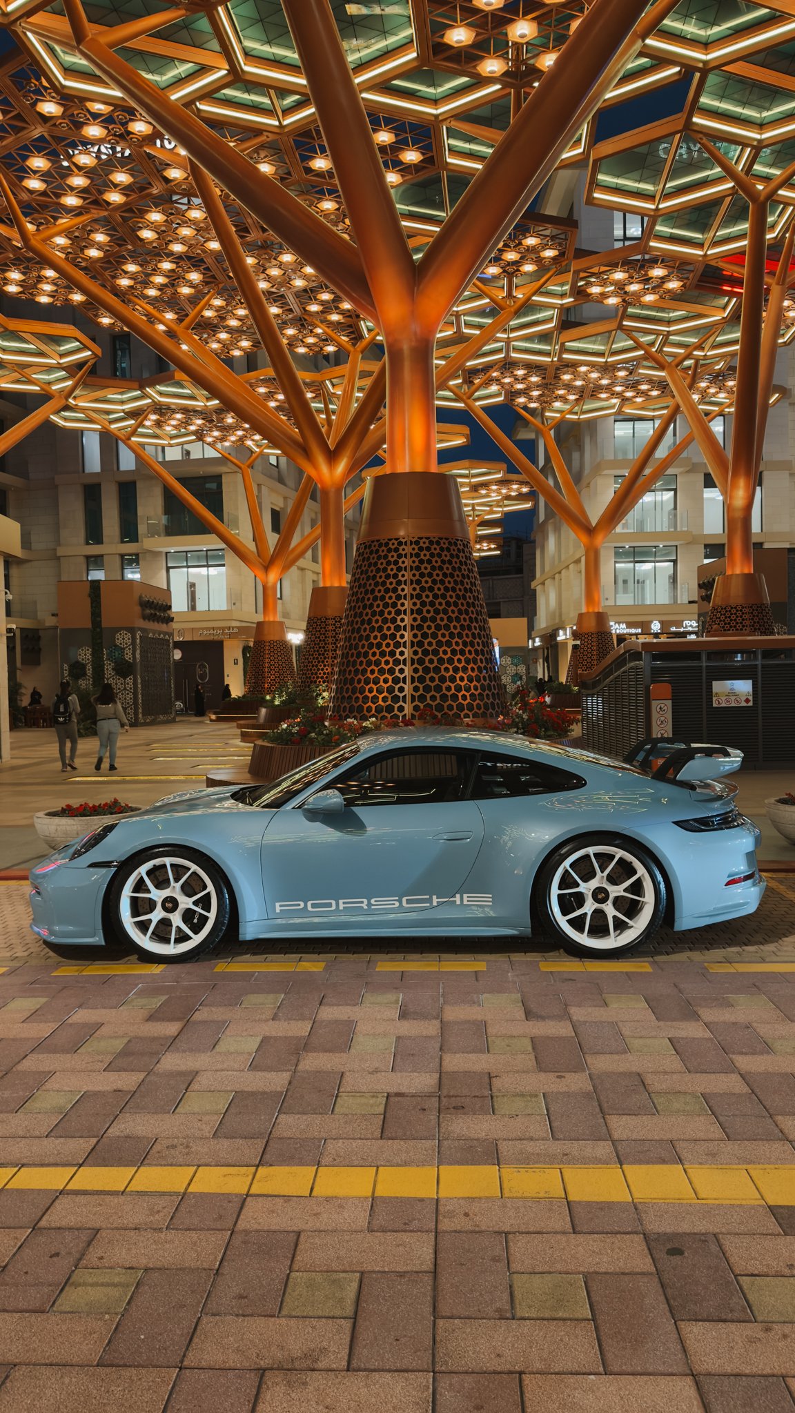 A pale blue sports car parked beneath a gold canopy, Gewan Island, Doha