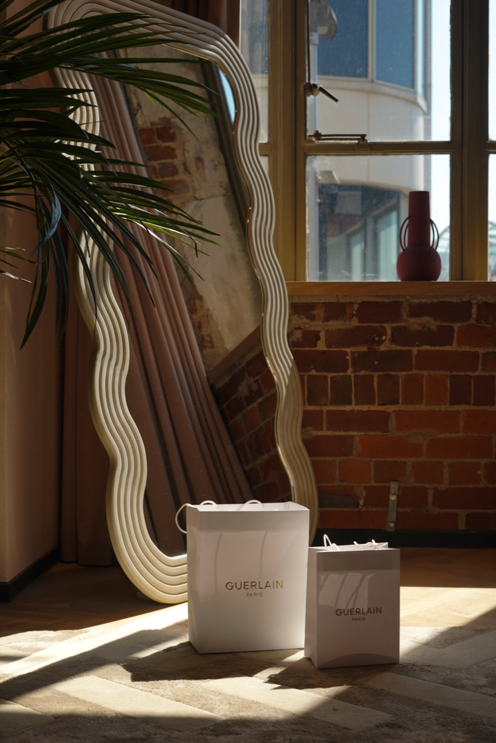 Guerlain paper bags in sunlight beside a mirror and exposed brick wall, Leeds