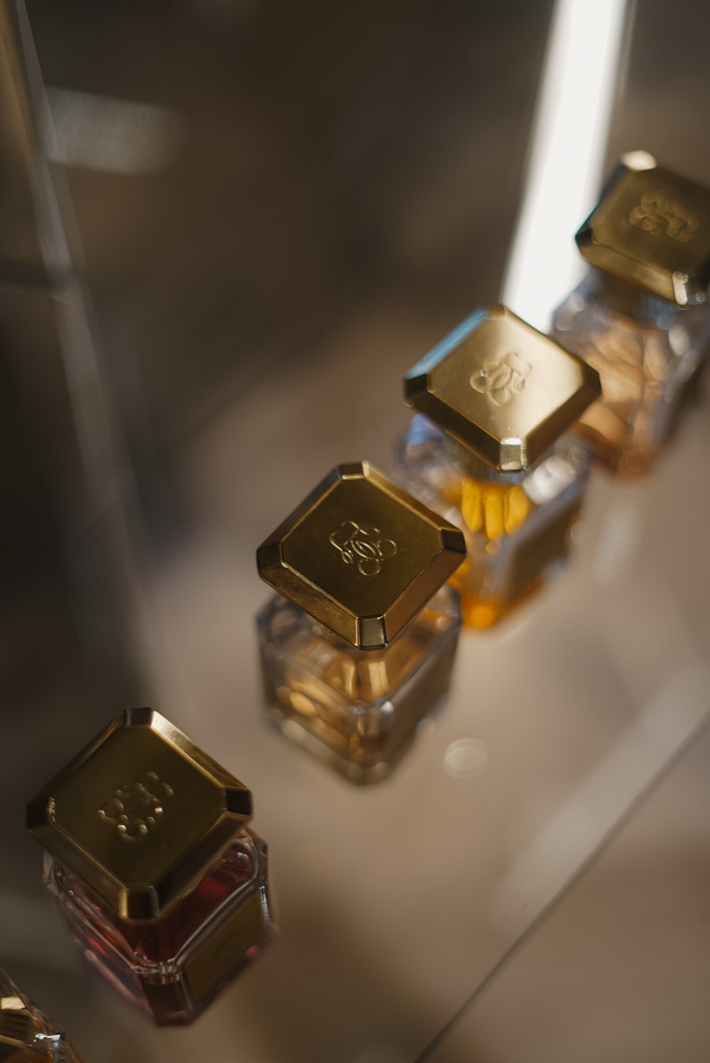 Gold caps of fragrance bottles seen from above in a lit cabinet, Guerlain, Leeds