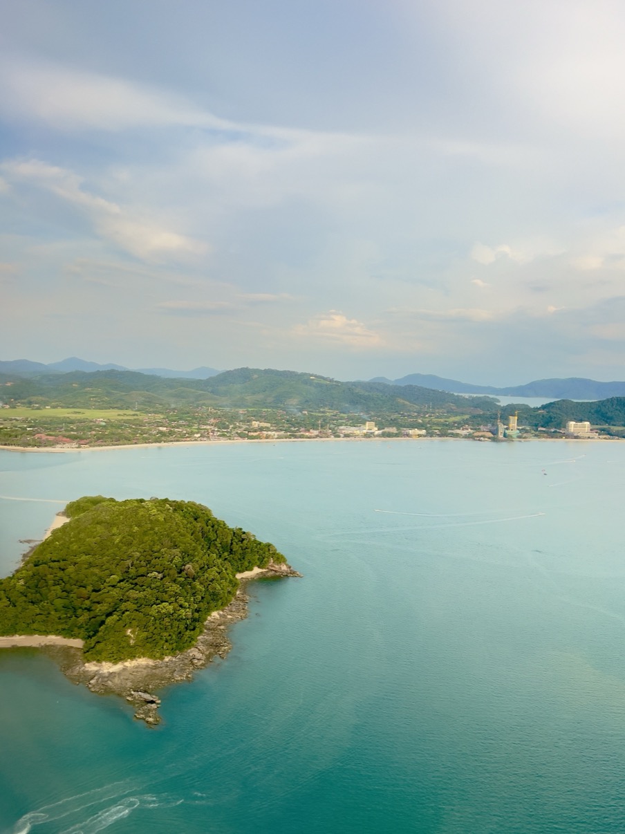 Aerial view over turquoise sea with forested island and mountain coastline, Langkawi