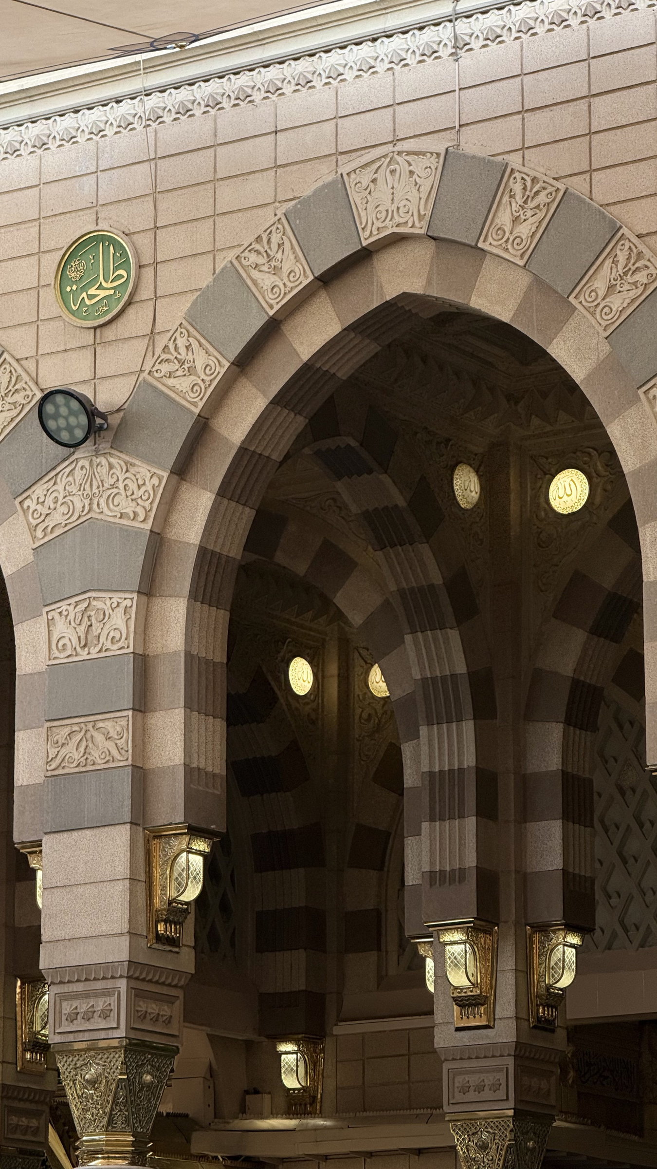 Arched entrance with striped stonework and gold wall lanterns, Madinah al-Munawwarah