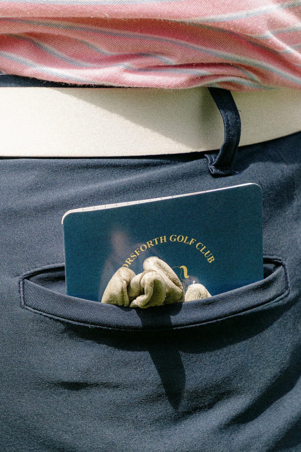 A club scorecard holder and glove in a back pocket, the cover photograph of Magnolia Classic