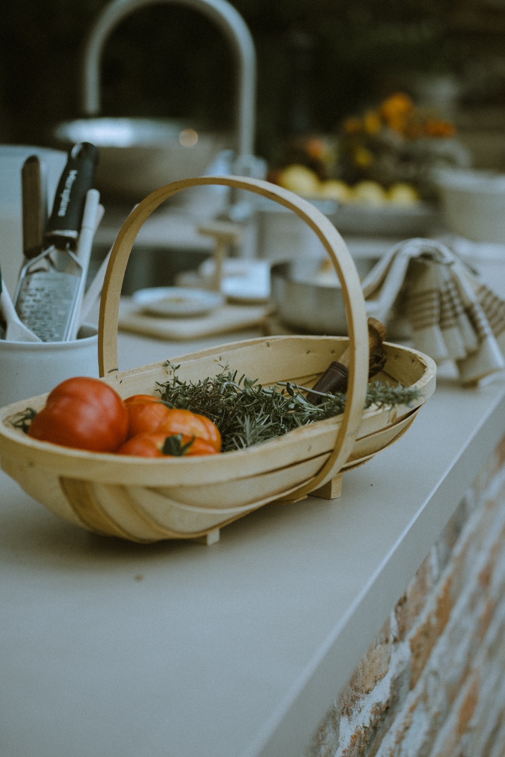 A wooden trug of tomatoes and cut herbs resting on the worktop, The Savills Garden, RHS Chelsea Flower Show, London