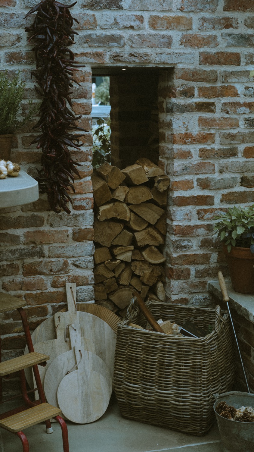 Logs stacked into a brick niche above a wicker basket of boards and tools, The Savills Garden, RHS Chelsea Flower Show, London
