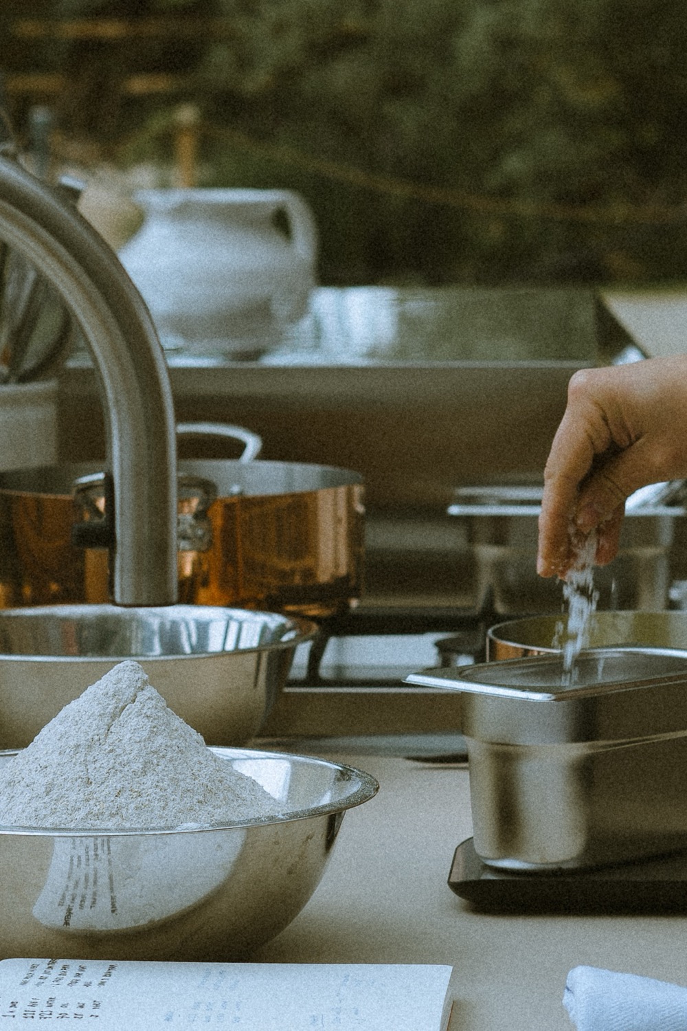 A hand sprinkling flour over a steel pan beside a bowl of flour, The Savills Garden, RHS Chelsea Flower Show, London