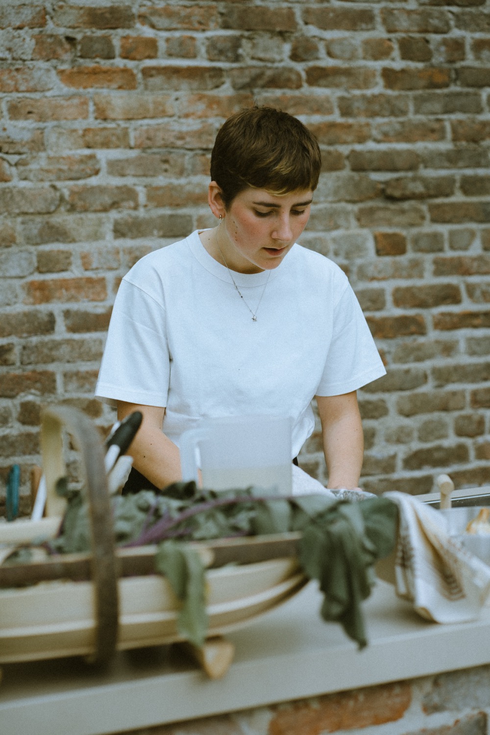 A cook working over a trug of cut greens against the brick wall, The Savills Garden, RHS Chelsea Flower Show, London