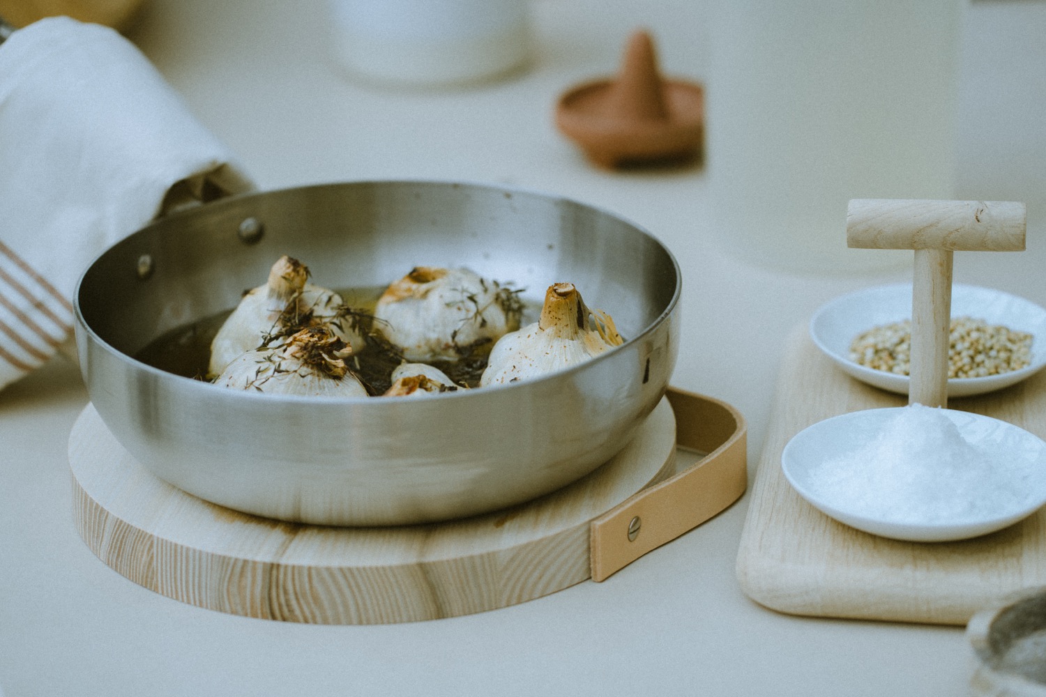 Roasted garlic in a steel pan beside dishes of salt and grain on a wooden board, The Savills Garden, RHS Chelsea Flower Show, London