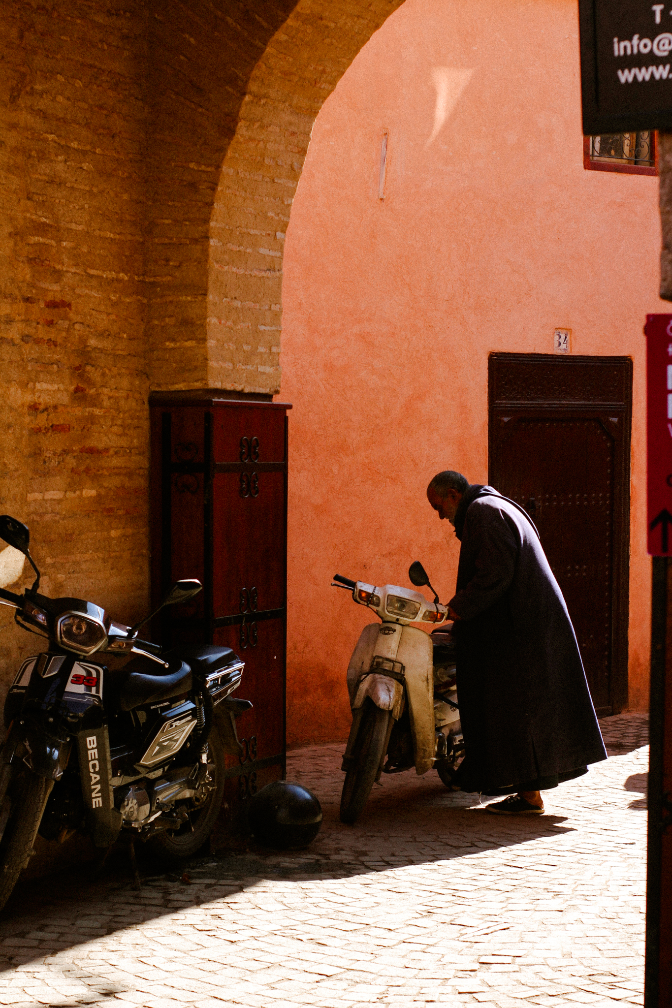 A man beside a scooter against a coral wall, Marrakech