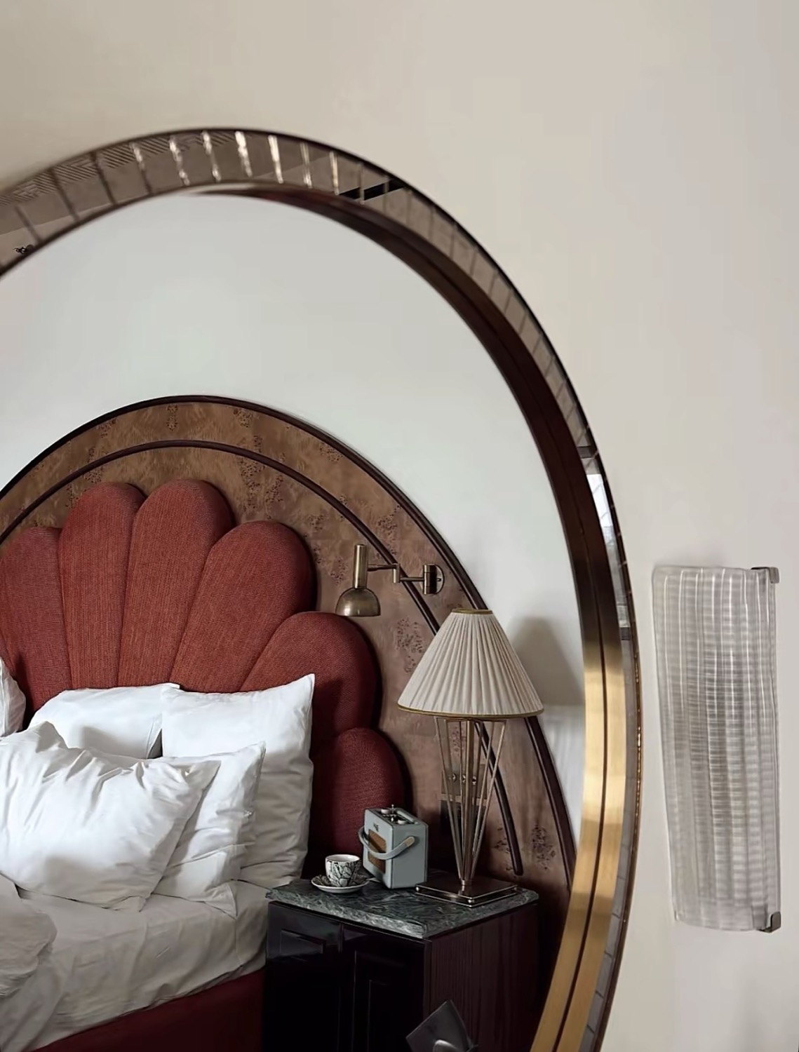 Art Deco hotel room reflected in a circular gilt mirror, scallop shell headboard in rose upholstery