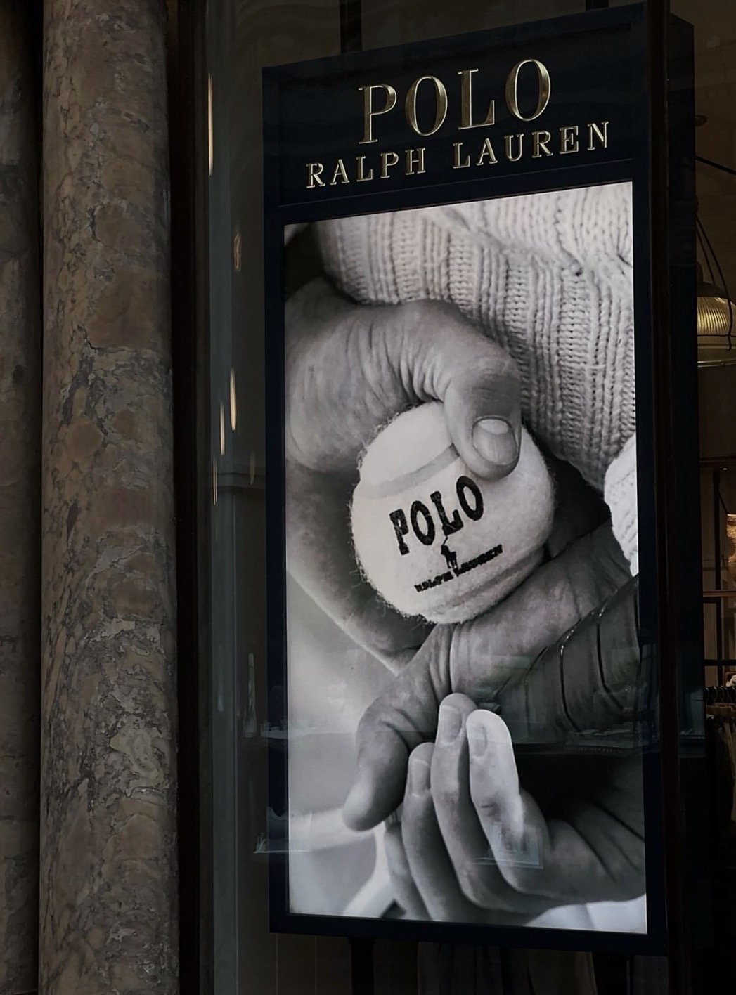 Polo Ralph Lauren storefront with campaign poster showing hands holding a polo ball, marble pillar beside it