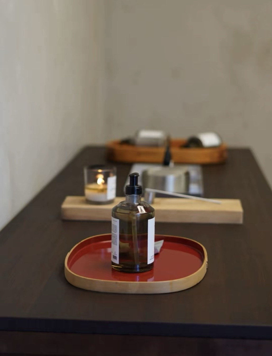 Spa treatment table with amber oil bottle on a red lacquer tray, candle and wooden tools alongside
