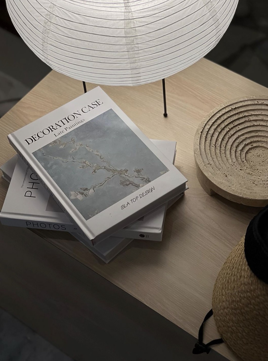 Stacked books including Decoration Case on an oak side table beside a rice paper floor lamp and travertine coaster