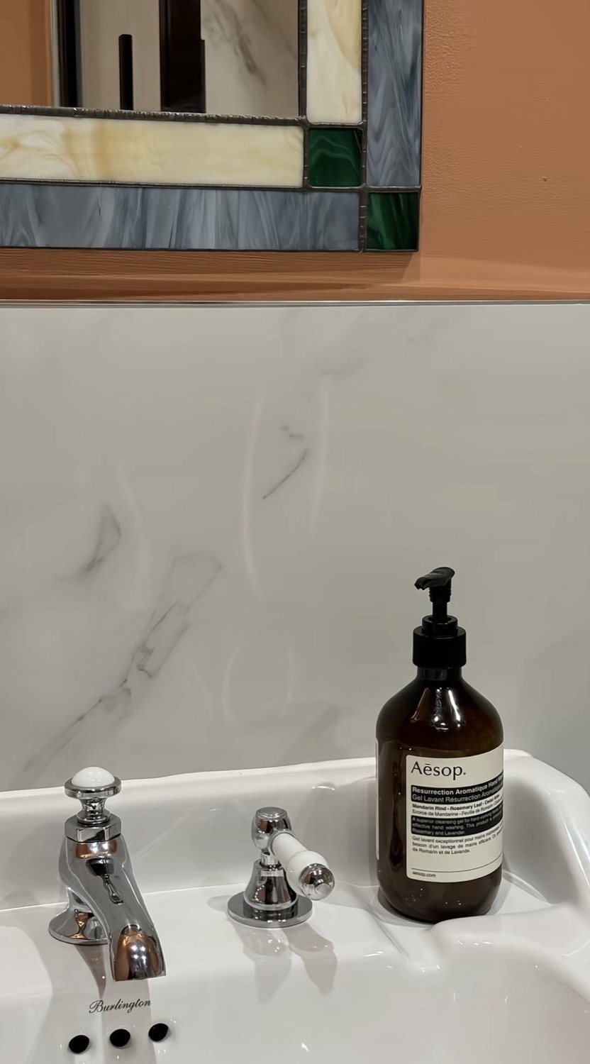 Burlington sink with Aesop Resurrection Aromatique bottle, stained glass art deco mirror above on a terracotta wall