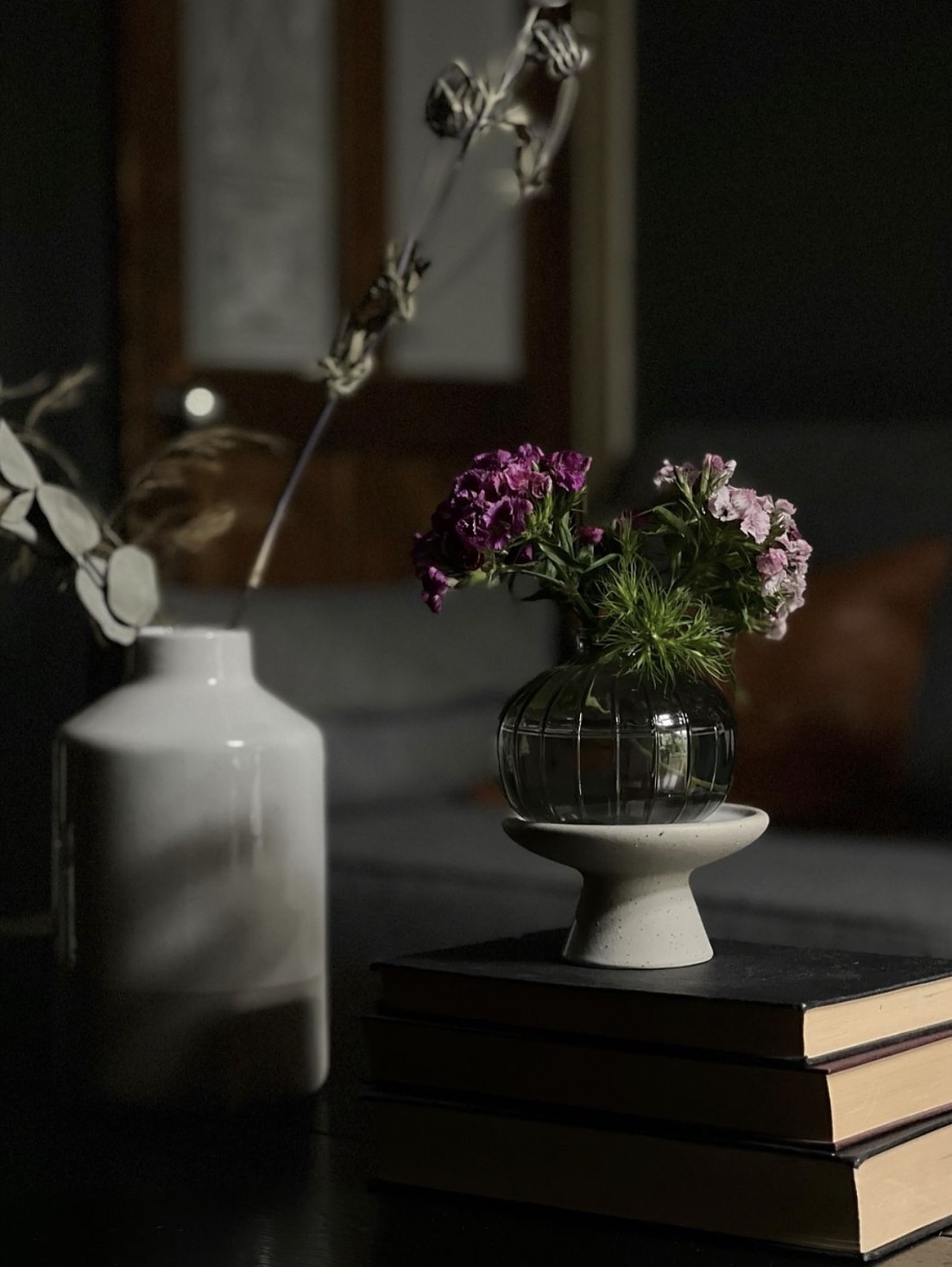 Purple and pink flowers in a glass vase on a concrete pedestal, dark background
