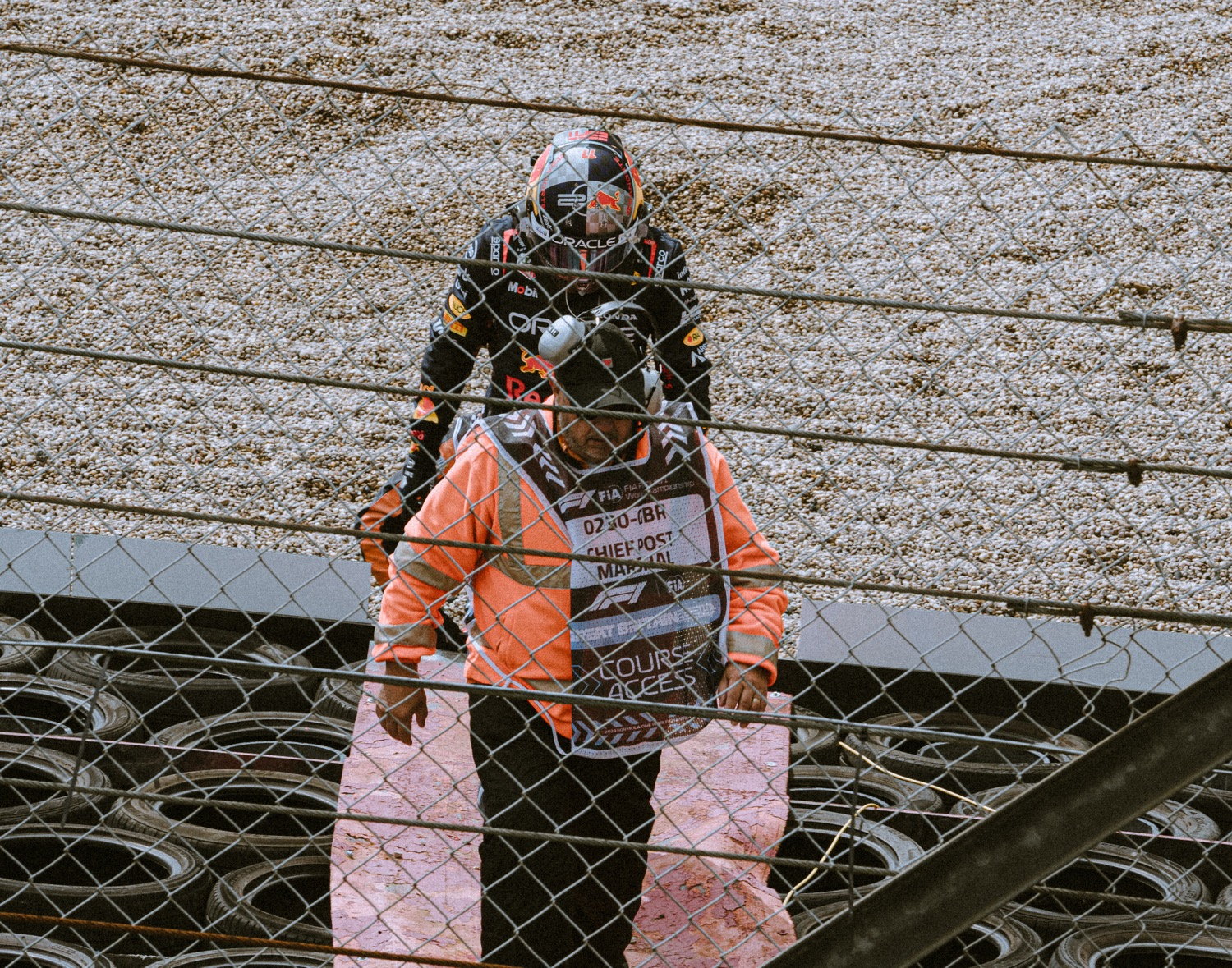 F1 driver climbing a barrier fence with a marshal assisting, grandstand behind