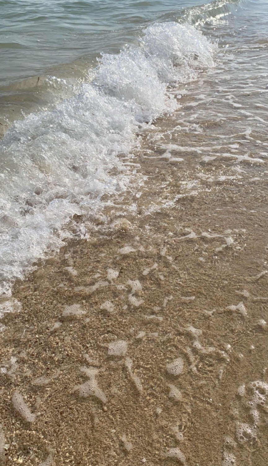 Wave retreating on a wide sandy shore, shallow water across flat beach