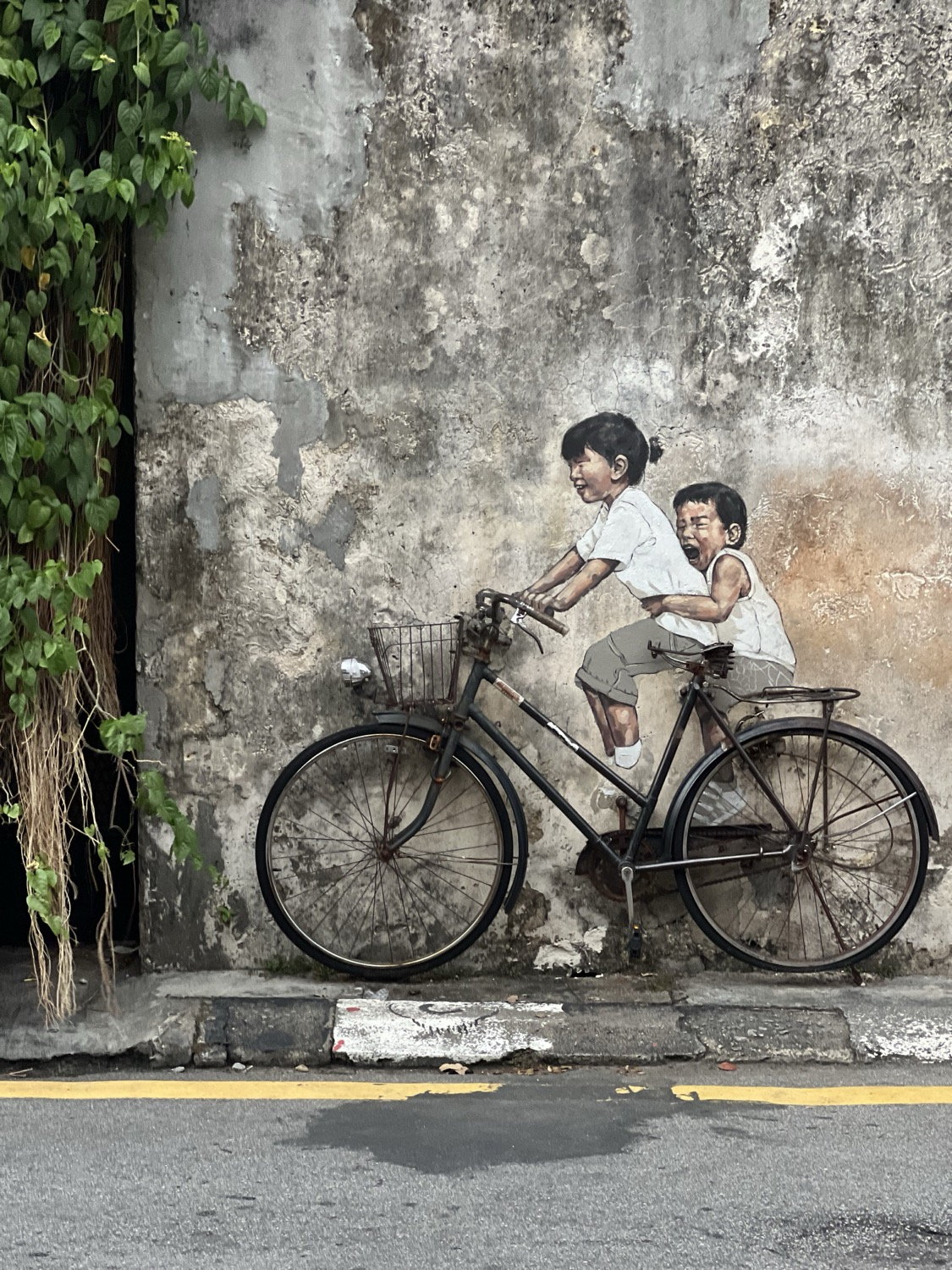 Penang street mural of children on a bicycle, painted on a weathered terracotta wall