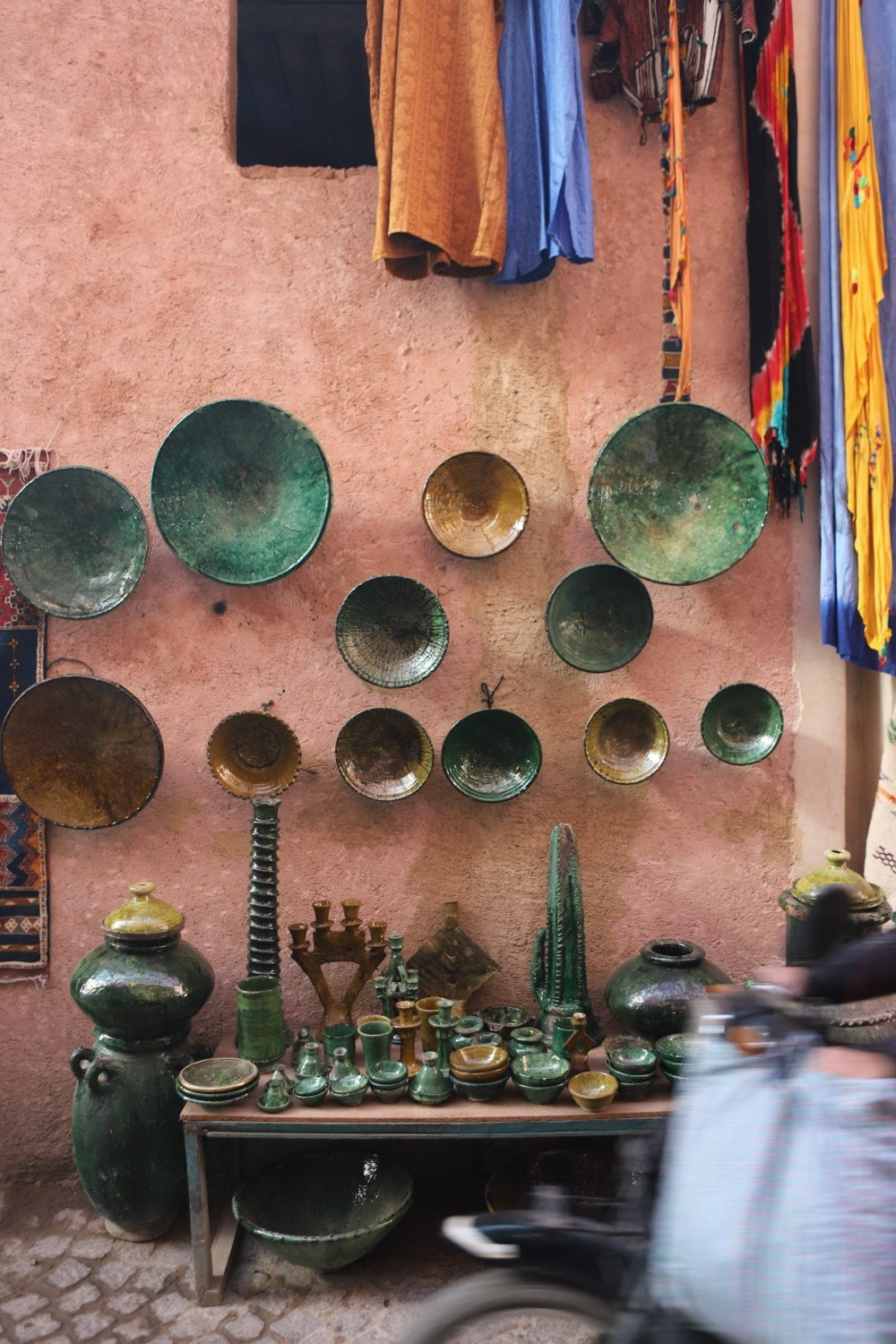 Green ceramic bowls arranged on a pink souk wall, scooter passing in blur, Marrakesh