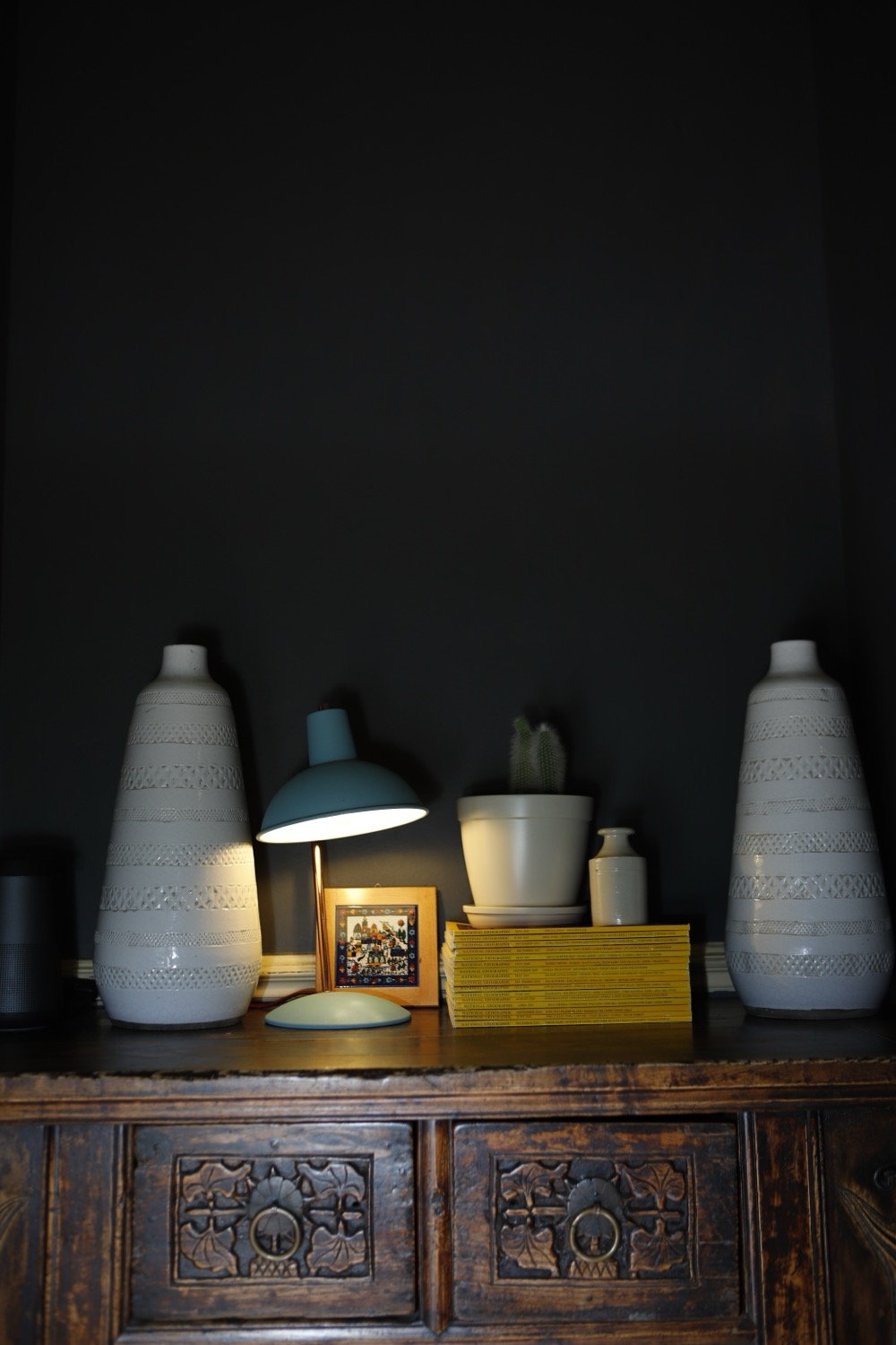 Dark carved sideboard with ceramic vases, small lamp and yellow books in a dim interior