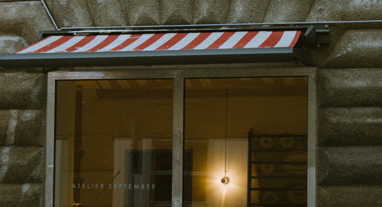 Atelier September café shopfront at night, red and white striped awning, warm interior light visible through the window, Copenhagen