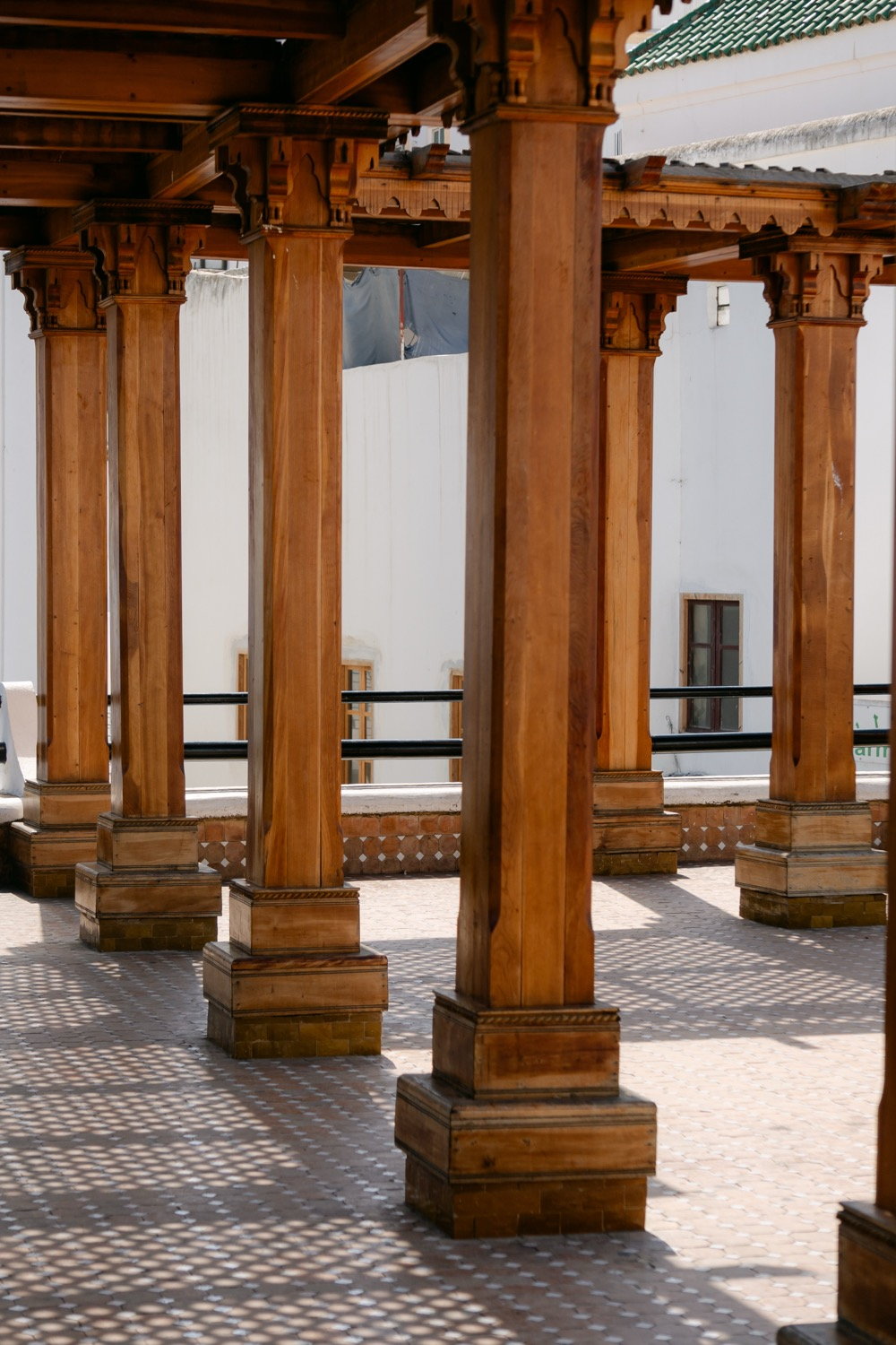 Row of carved wooden columns inside a mosque inner courtyard, zellige tile floor, Marrakesh