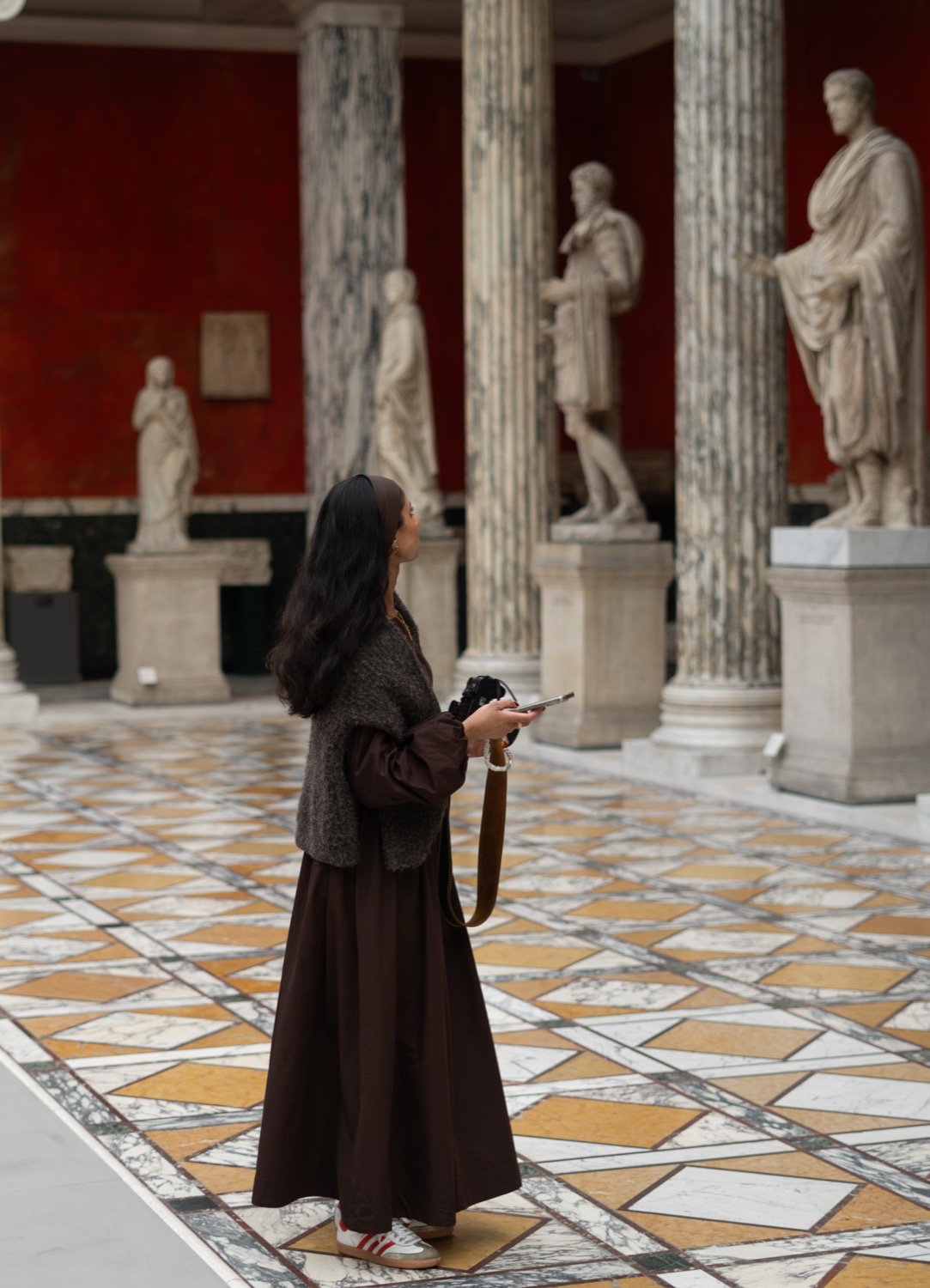 Woman standing in a classical sculpture hall, marble columns and Roman statues on a mosaic marble floor, Copenhagen