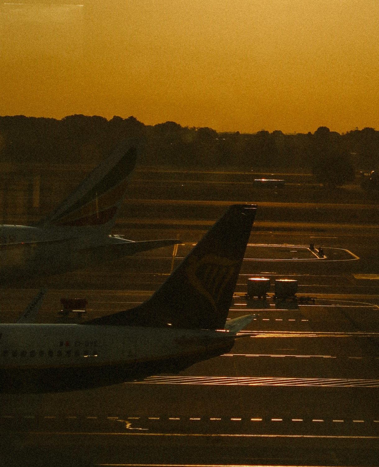 Aircraft tails silhouetted against a deep amber sunset sky on an airport tarmac