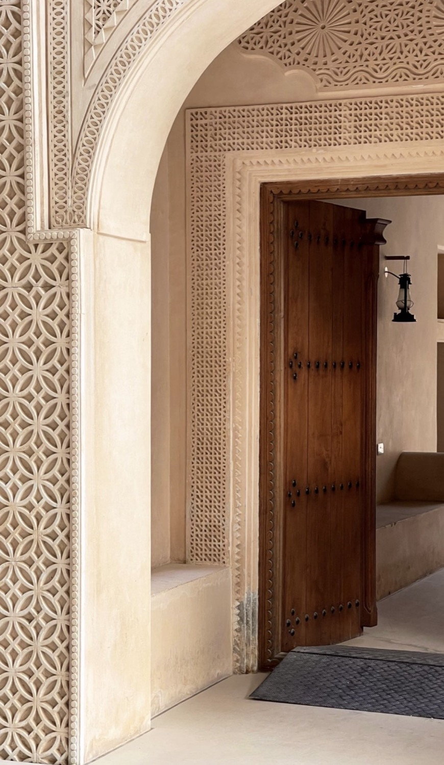 Ornate carved plaster lattice arch surround with geometric pattern and dark carved wooden door beyond, Doha