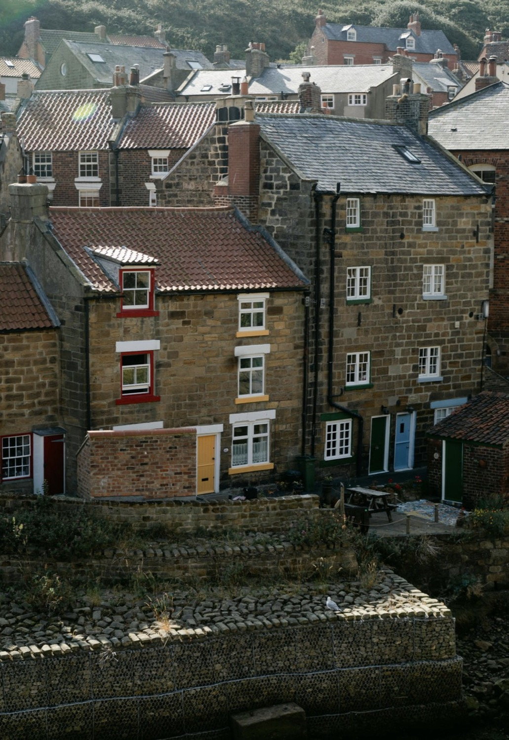 Stone and brick village houses stacked on a hillside with slate rooftops and red window frames, Yorkshire