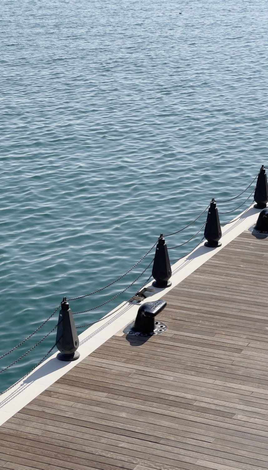 Wooden jetty boardwalk edge with dark mooring bollards and chain, turquoise water alongside