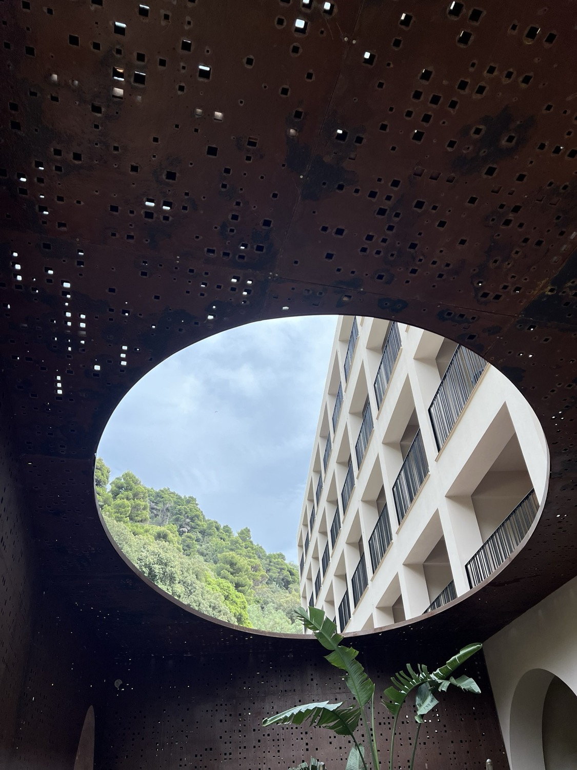 Looking through an oval cut-out in a perforated Corten steel wall to sky and rainforest canopy beyond, Langkawi