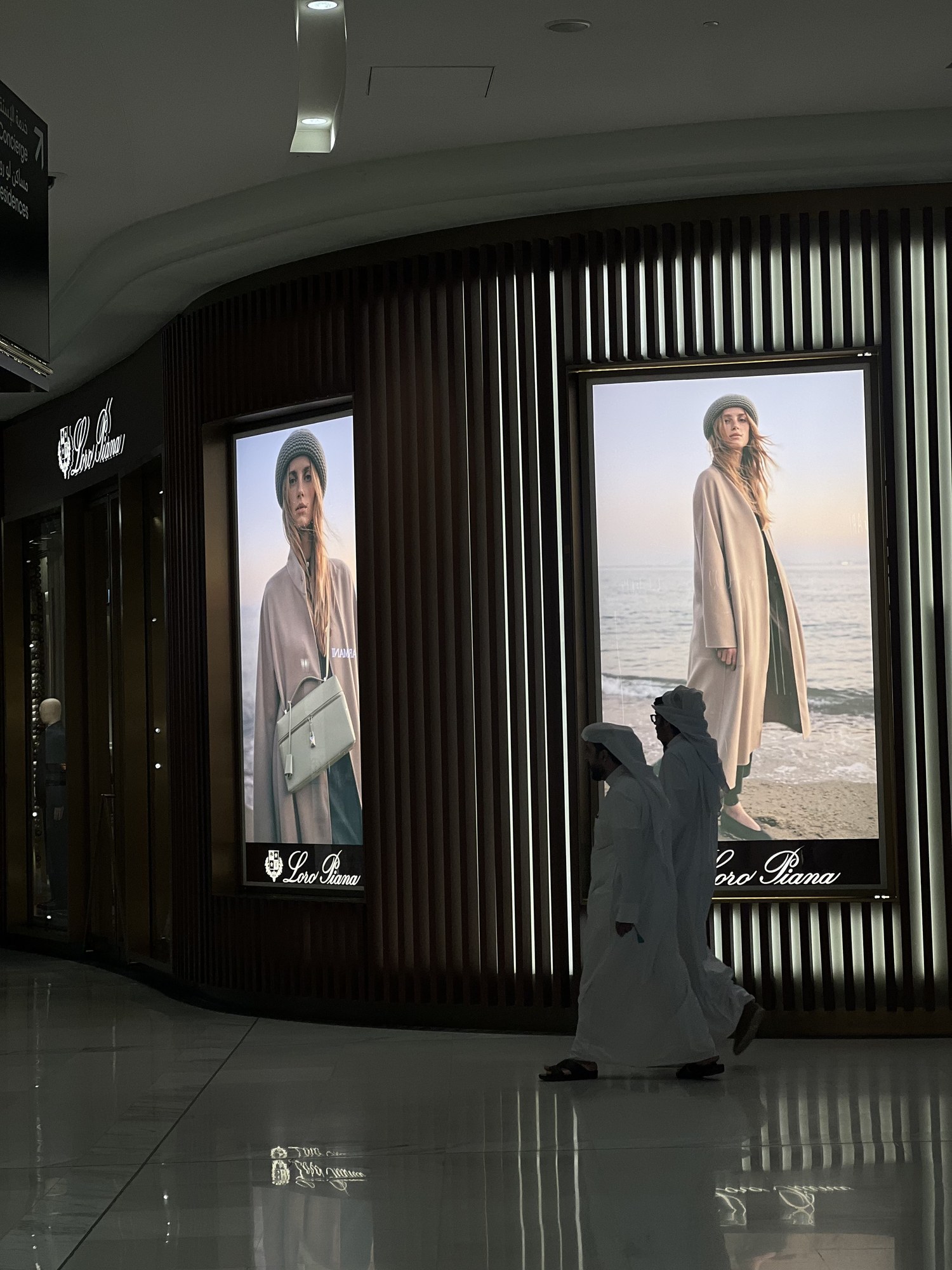 Loro Piana screens glowing at night as a figure in a white thobe passes