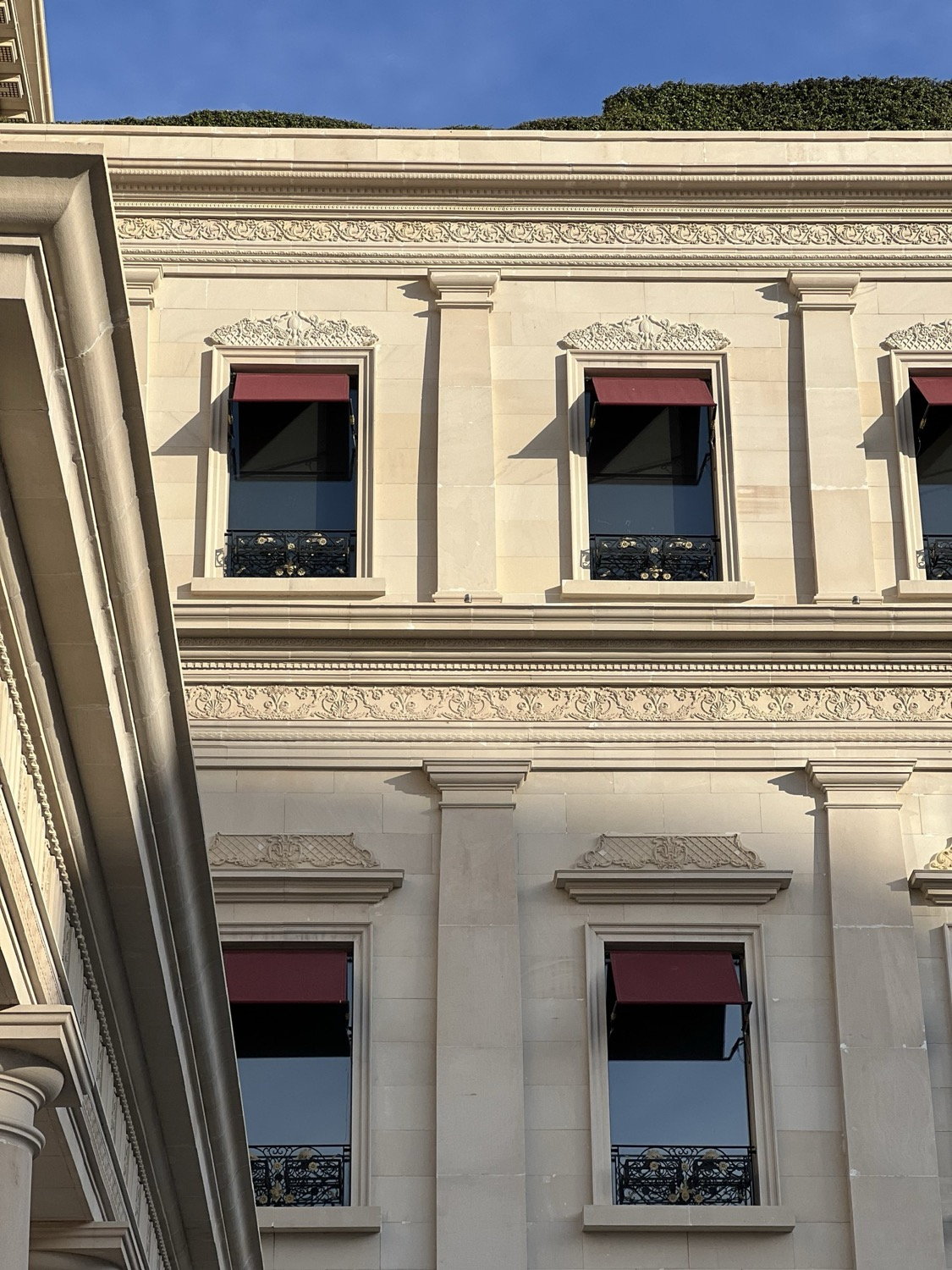 Haussmann-style stone facade seen from below, ornate window surrounds with dark shutters, blue sky, Paris
