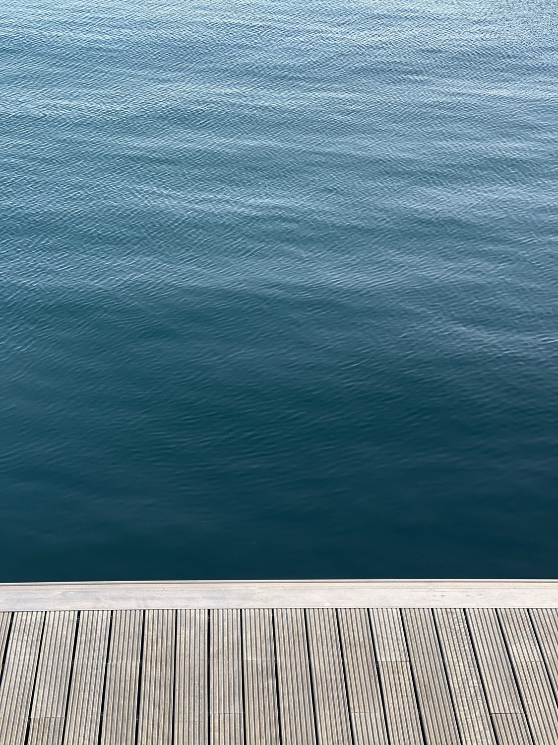 Overhead view of dark teal water beside a wooden boardwalk deck, minimal composition